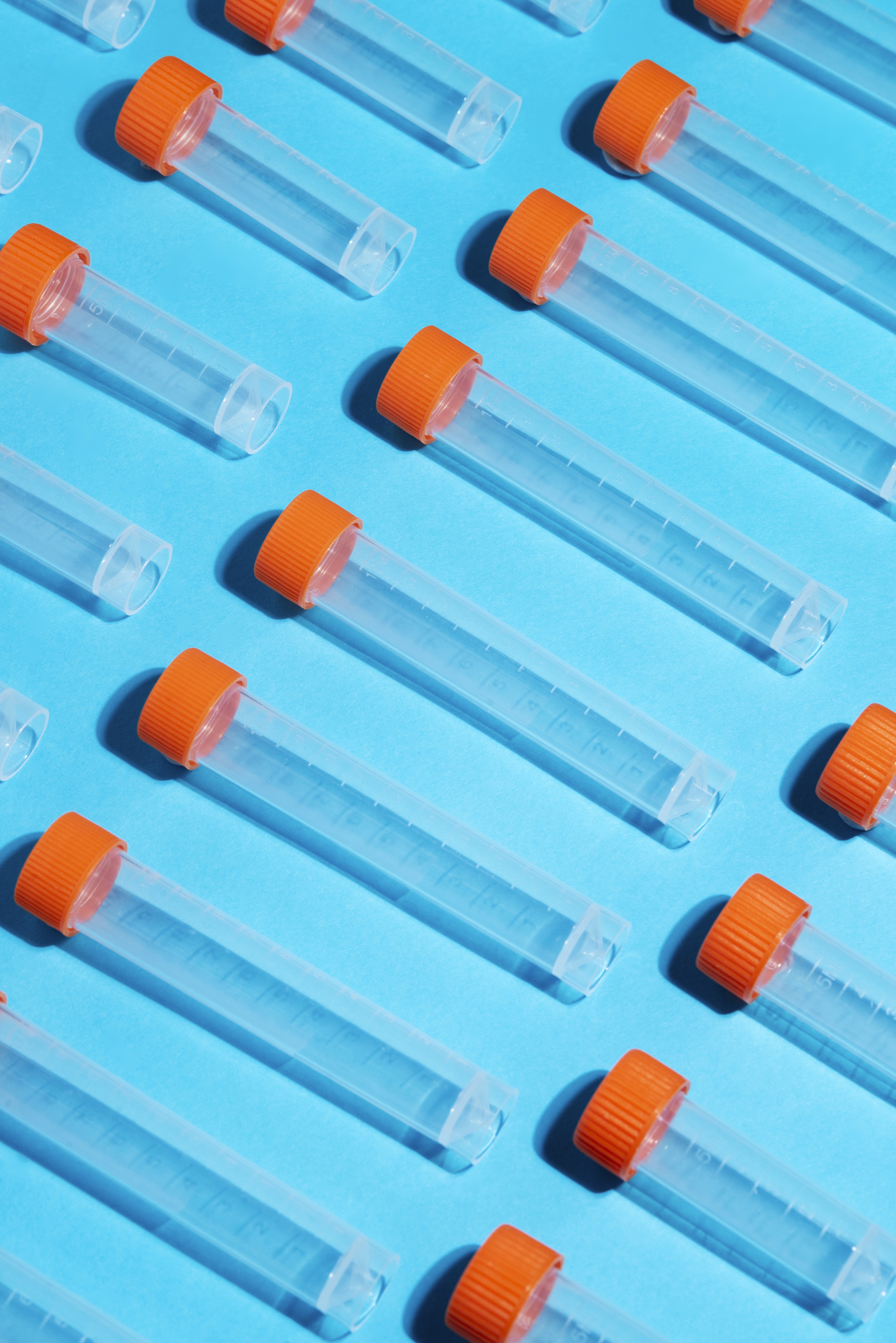 Rows of clear plastic test tubes with orange caps arranged on a blue background.