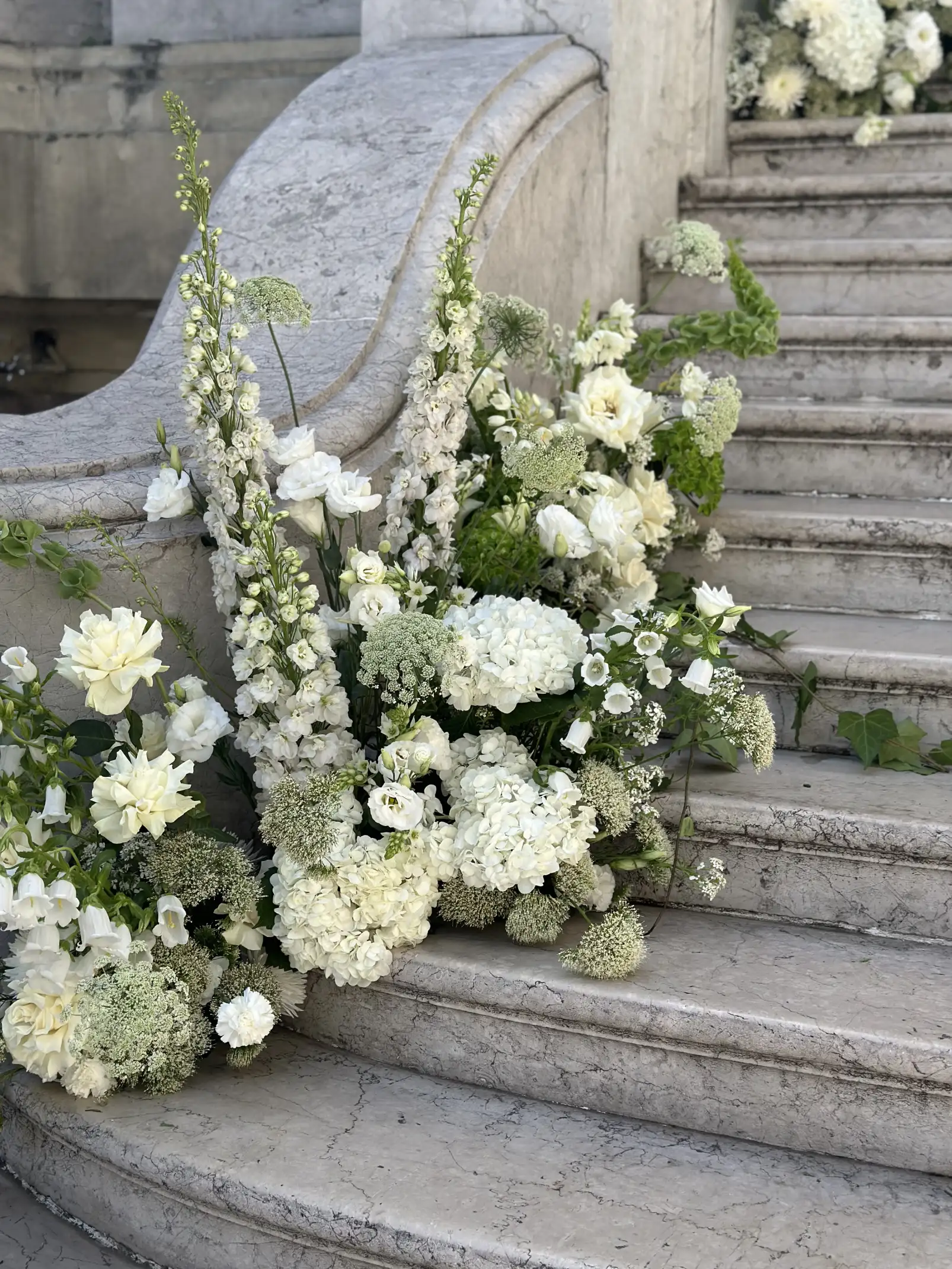 Arreglo floral blanco con textura orgánica sobre escalinata de mármol para ceremonia clásica, evocando elegancia atemporal.