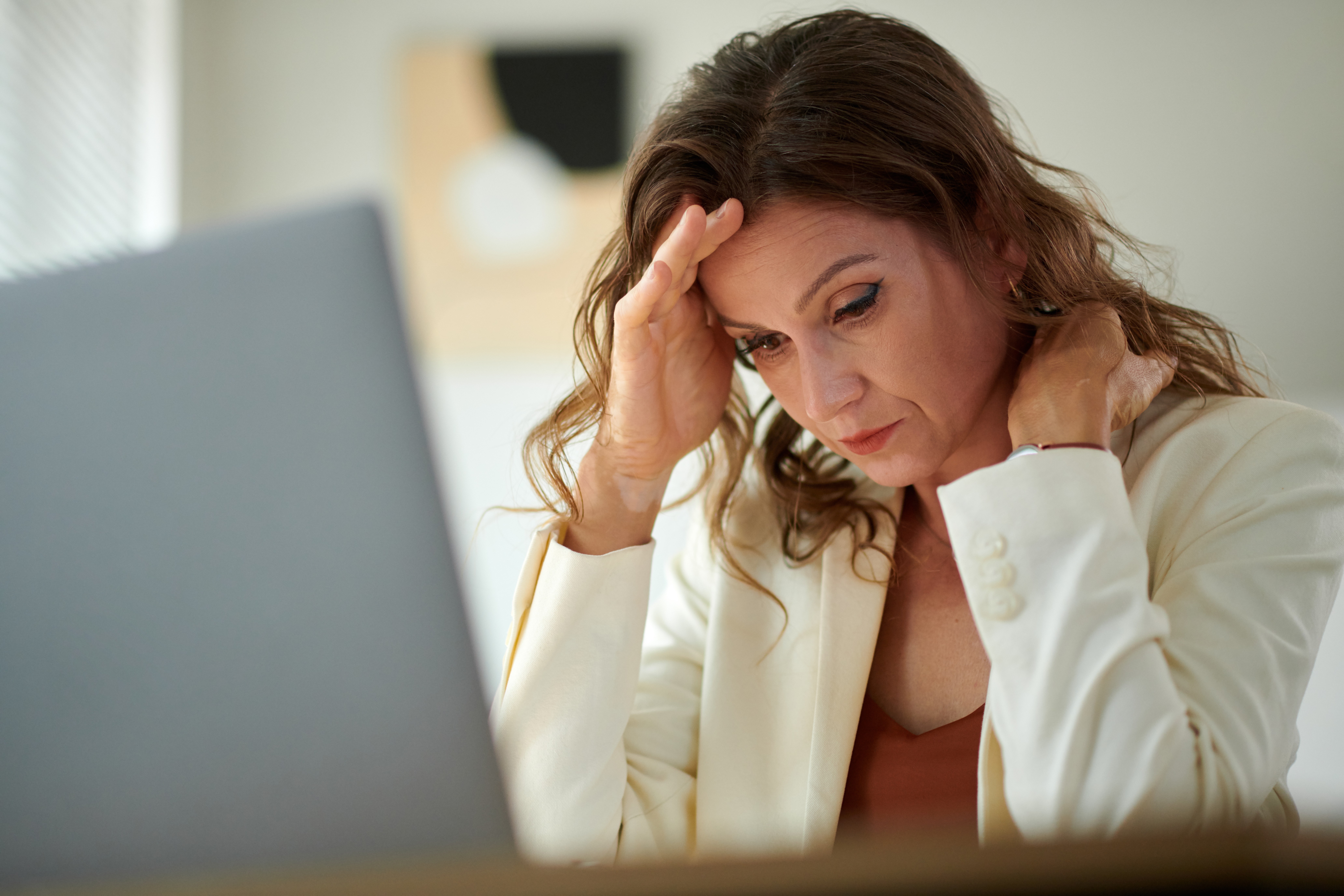 A woman sitting near a window, holding a mug and looking reflective.