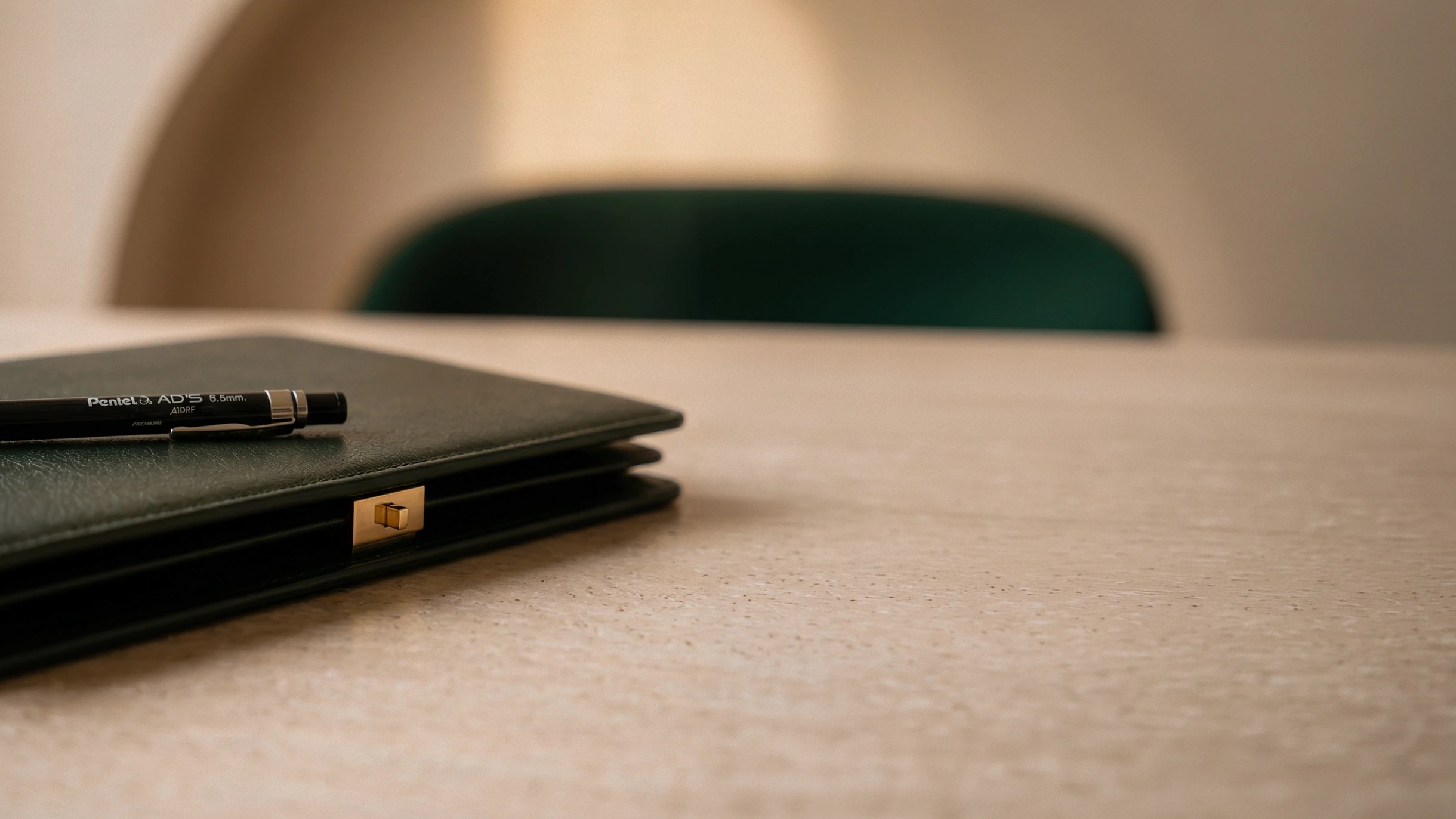 Close-up of a designer's green leather presentation folder and drawing pen on a modern wooden table inside the Shaun Leane independent atelier.