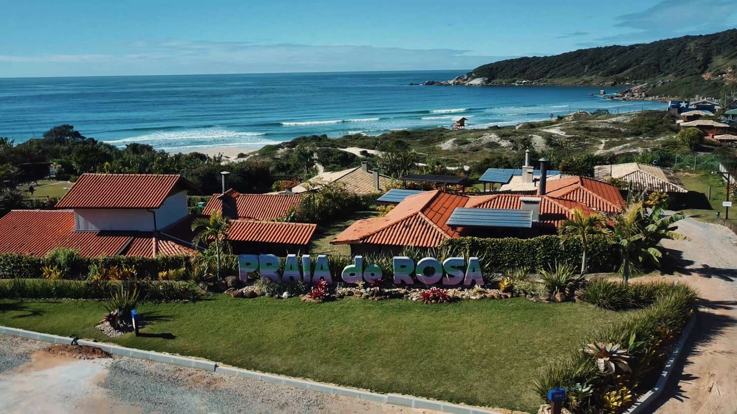 Foto aérea mostrando letreiro escrito "Praia do Rosa" com a orla ao fundo
