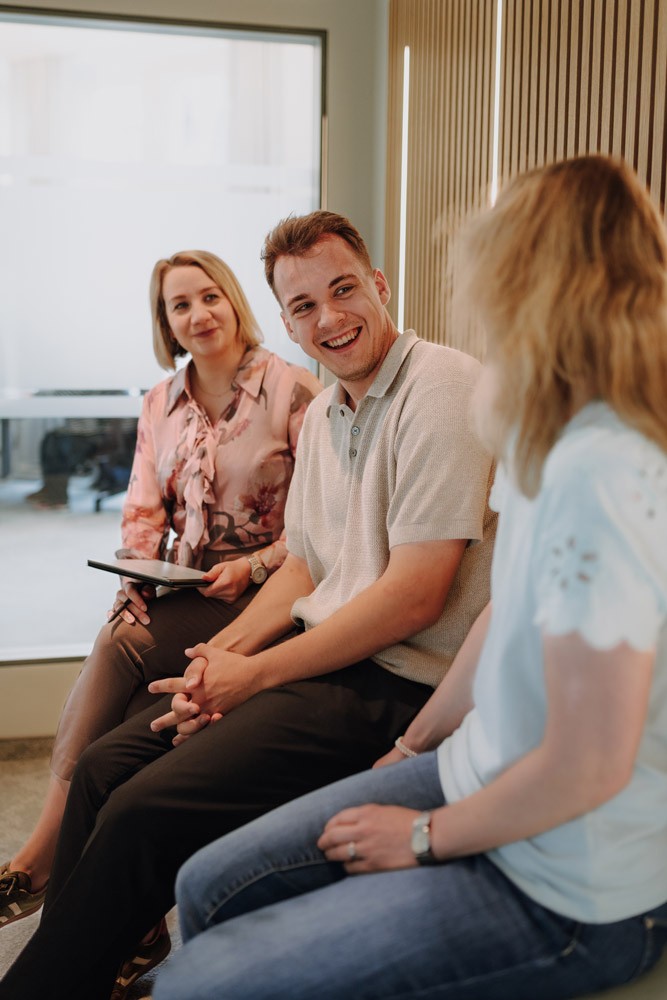 Weibliche Geschäftsführerin und zwei Personen sitzen gemeinsam an einer Bank und besprechen Unterlagen in einem hellen Büro von SLB.