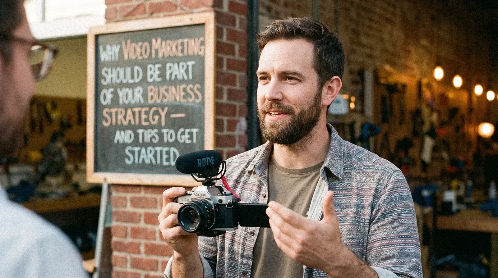 Bearded man filming video marketing strategy tip outside workshop with Canon camera Rode mic - chalkboard sign
