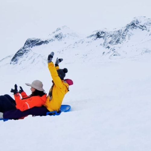 Люди катаются на санках с заснеженного холма на леднике