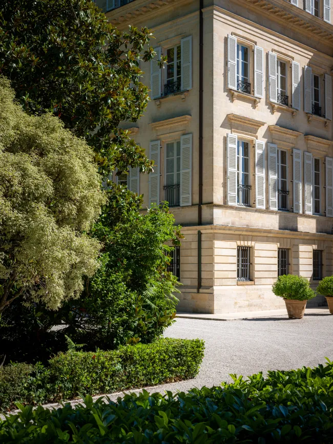A corner of a building with large windows, surrounded by greenery and a neatly manicured pathway.