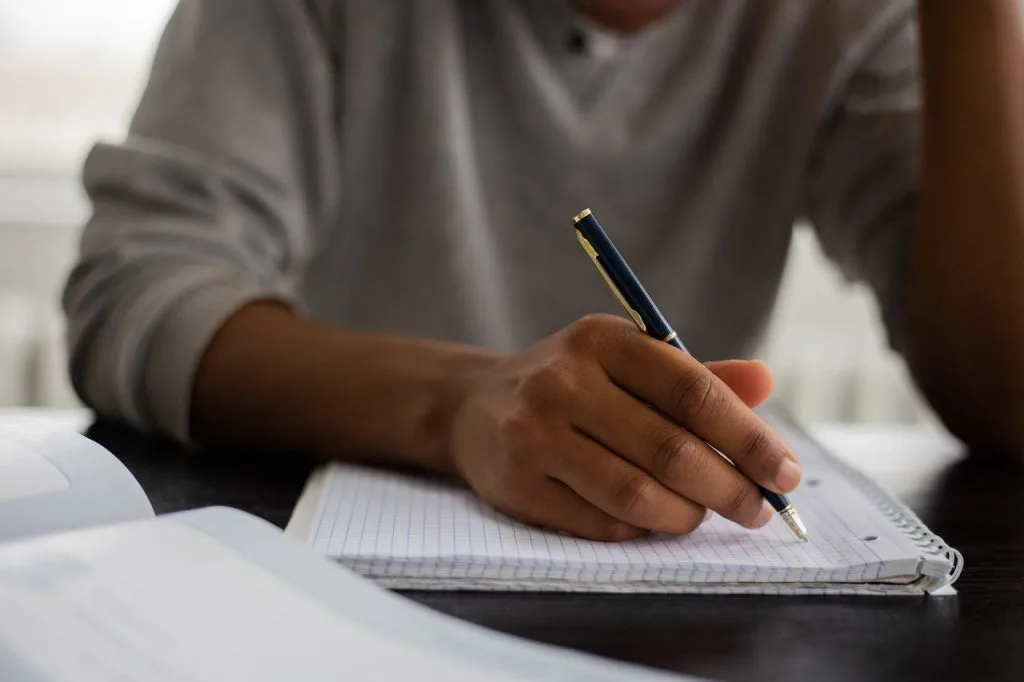 High school student writing notes in a notebook during RISE Research summer program, focusing on academic research, critical thinking, and subject mastery.