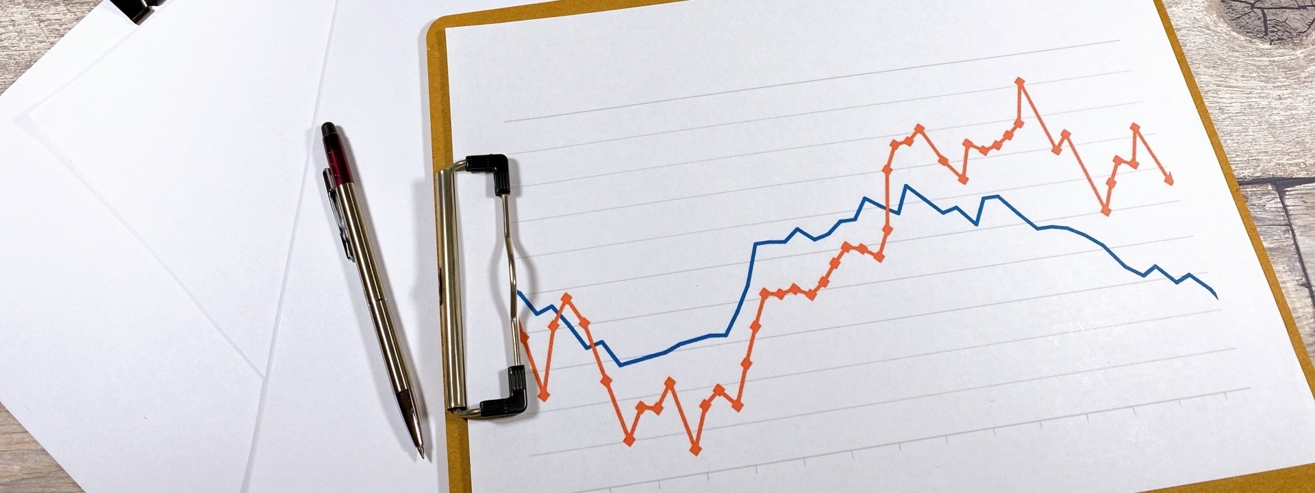 グラフの描かれたクリップボードとオフィス文具が並ぶ作業デスク