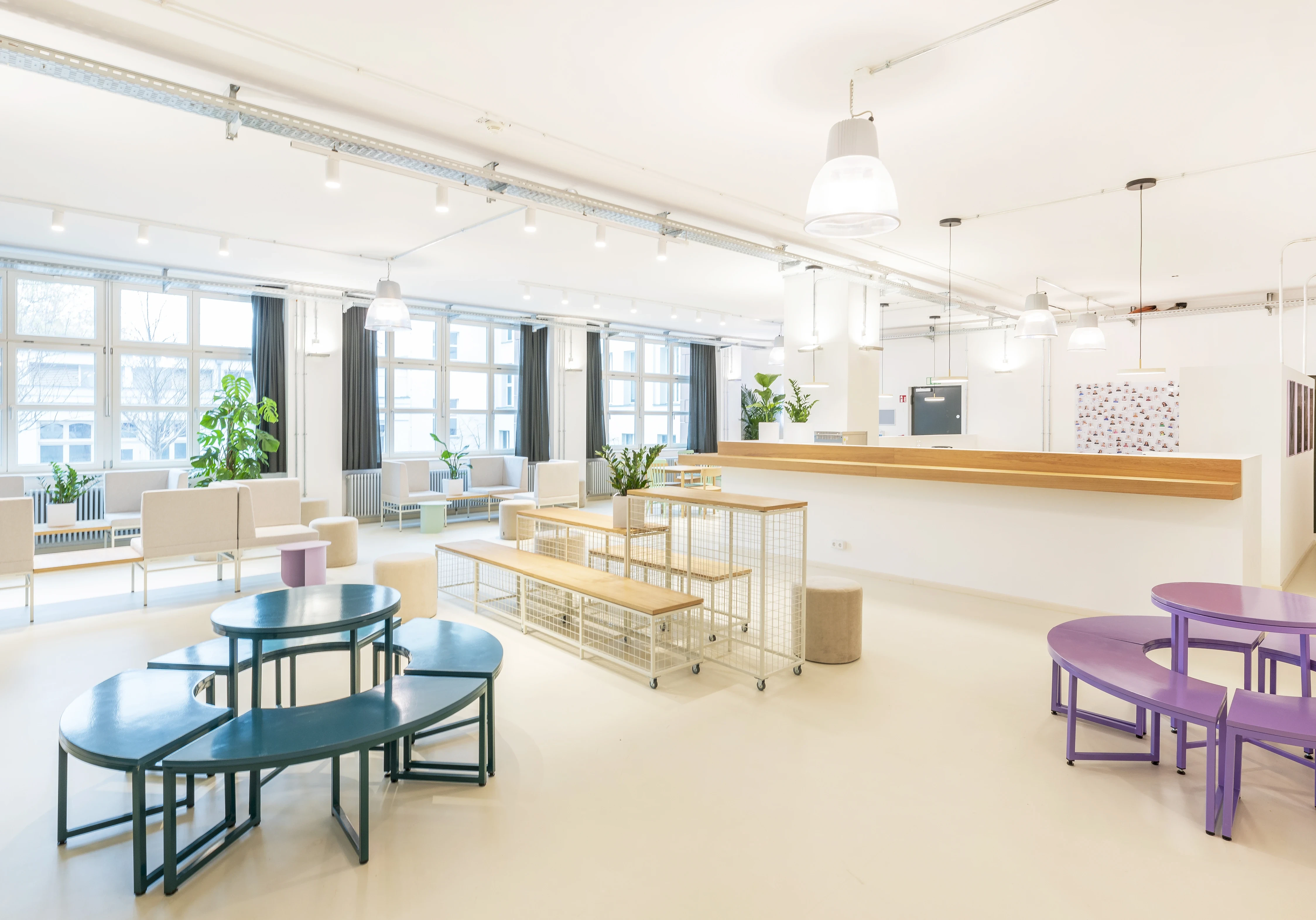 Multi-zone interior at ELEMENT with petrol-blue and purple round bench groups, birch benches with white mesh bases, a long reception counter with wood top and a seating lounge by the windows.