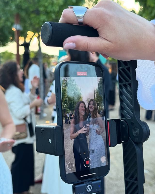 Young woman with short, dark hair and a yellow sweater looks serious, surrounded by hands holding smartphones, conveying intrusion and tension.