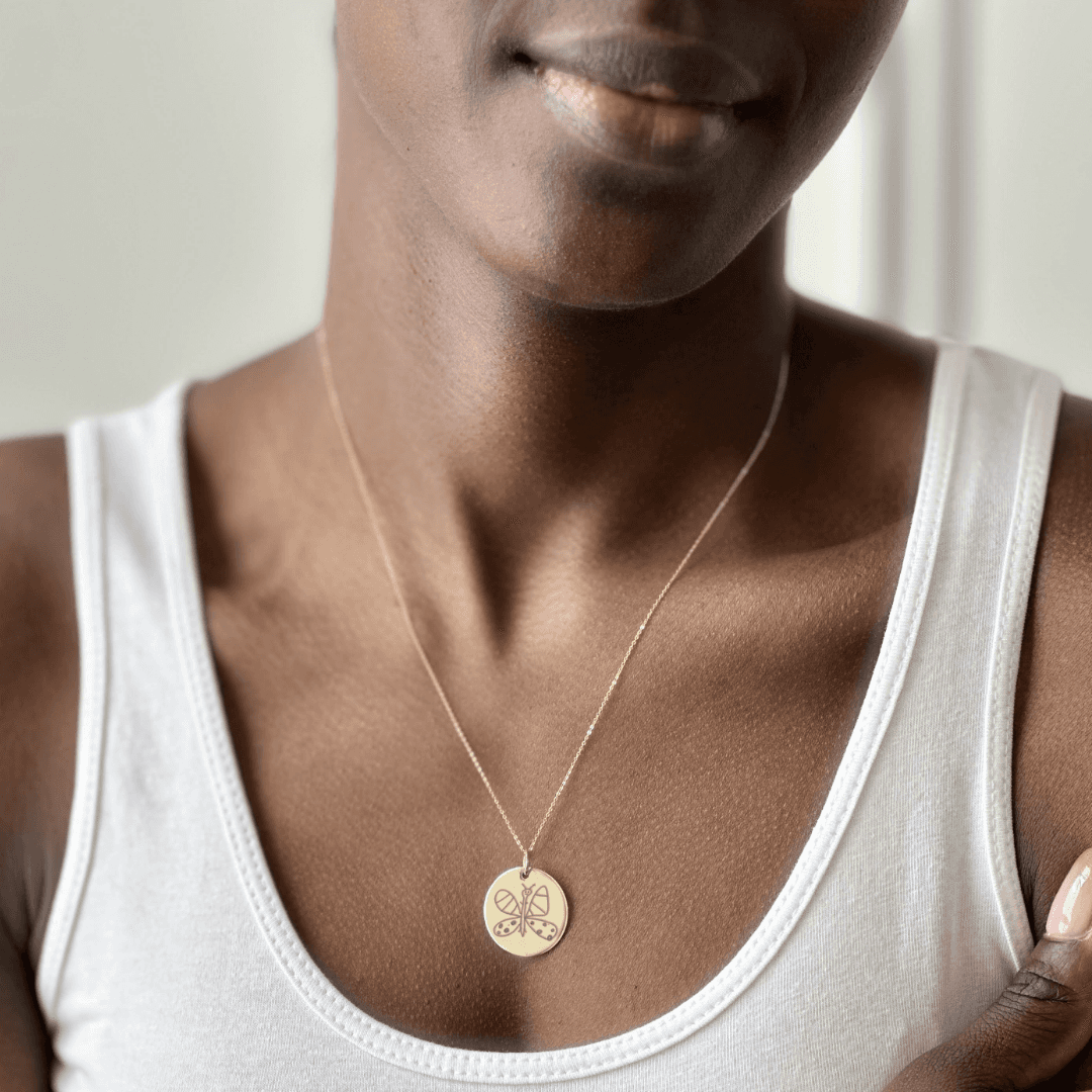 Woman wearing a gold Night Sky Doodle pendant of a butterfly drawn by a child.