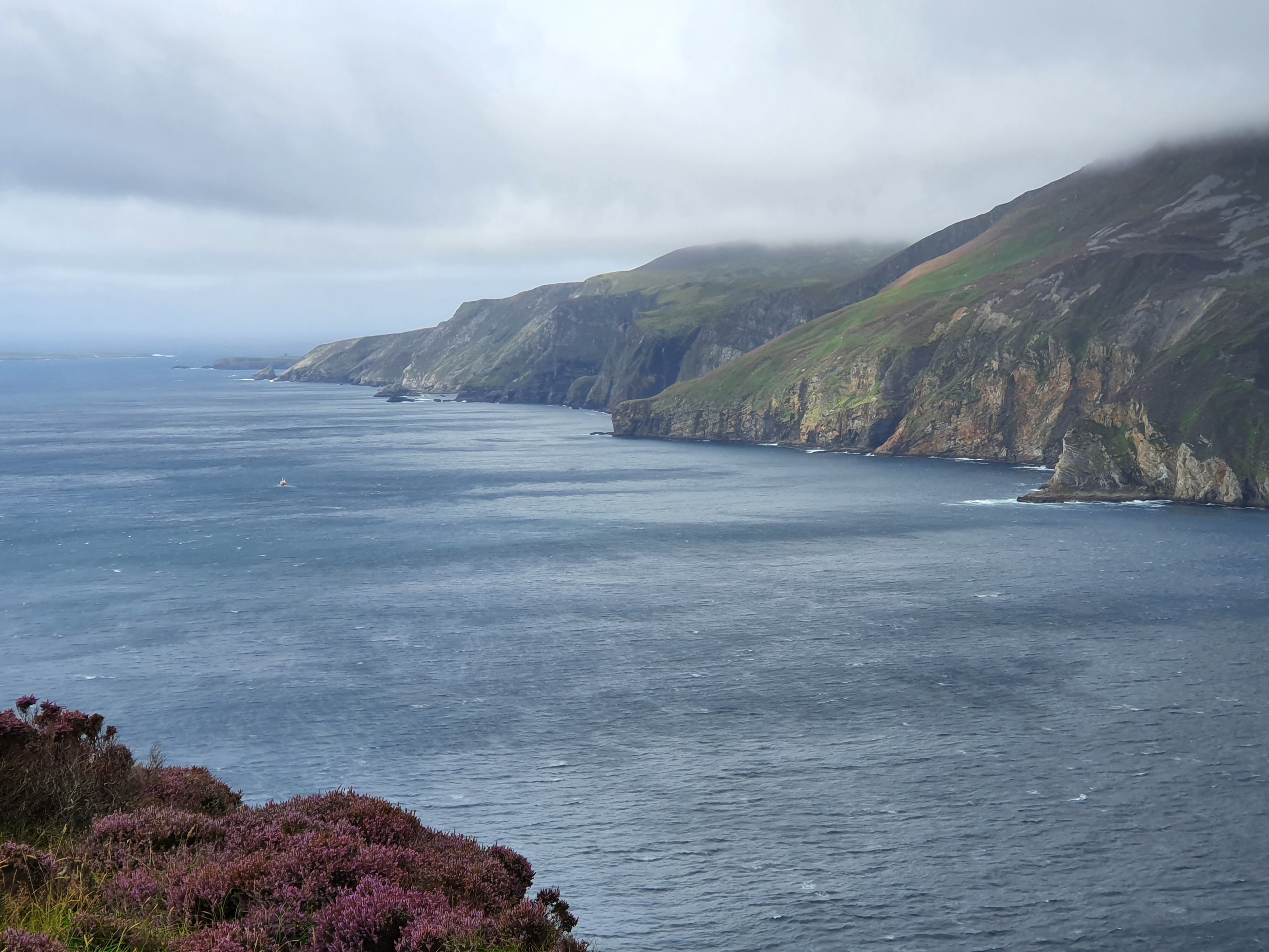 A scenic coastal view with rolling hills and calm waters under a cloudy sky.