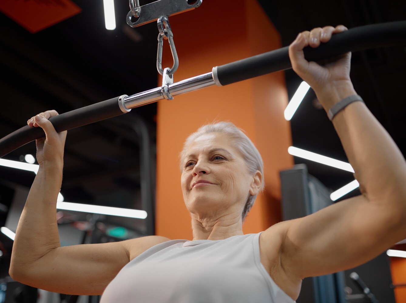 older woman using a machine to do lat pulldown weight exercises for weight loss at the gym