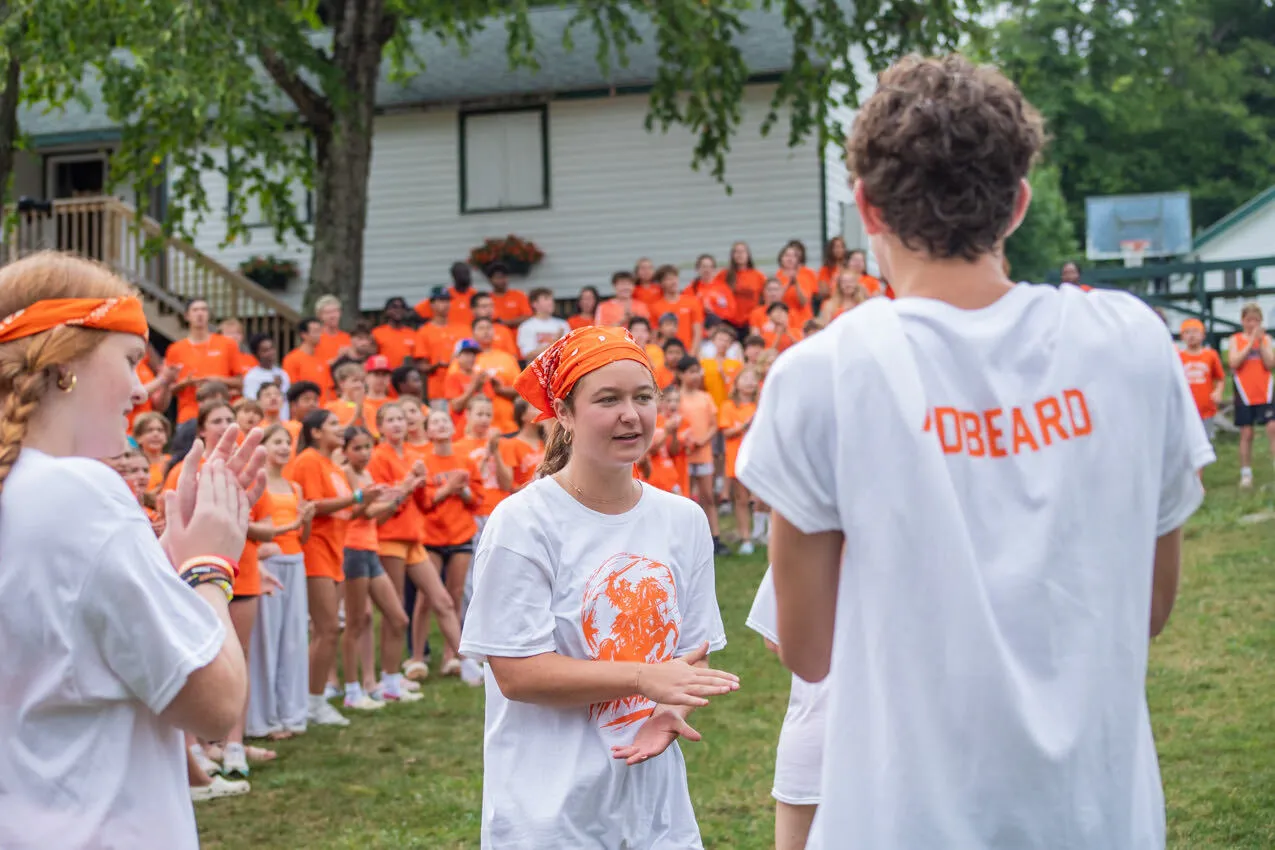 Campers in orange gathered on the lawn for a camp event at Camp Lenox
