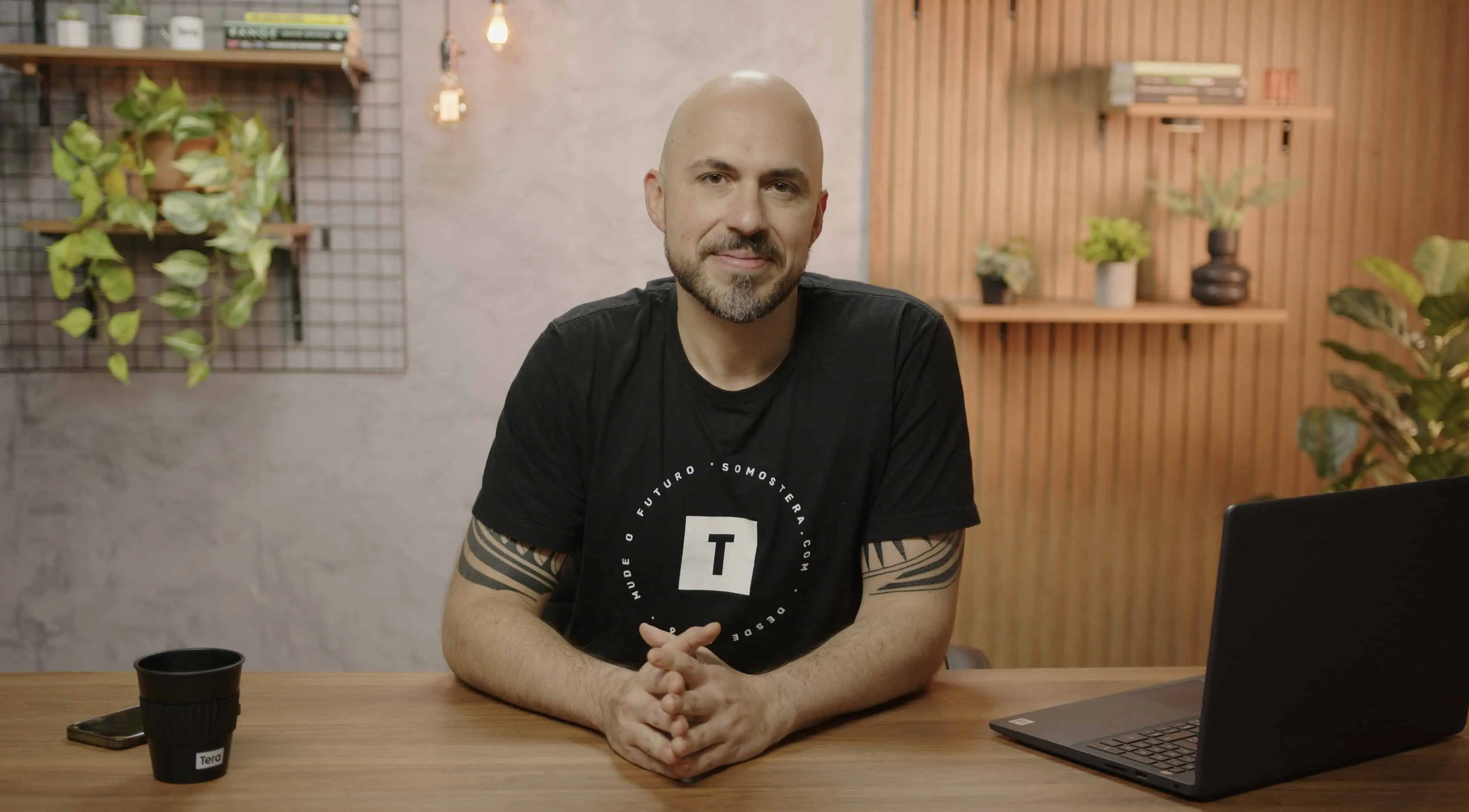 Leandro Herrera sentado em uma cadeira, sorrindo, com uma paisagem urbana e uma planta visíveis ao fundo.