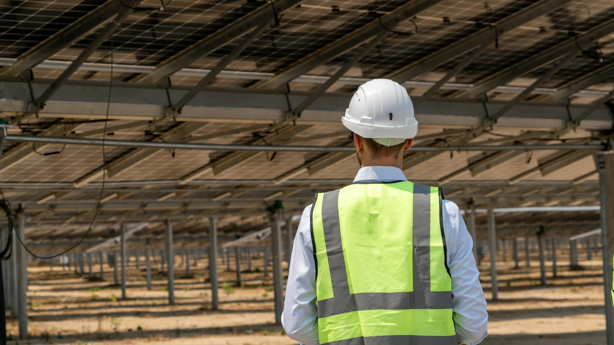 A worker in a hard hat and safety vest walking under the panels of a solar farm