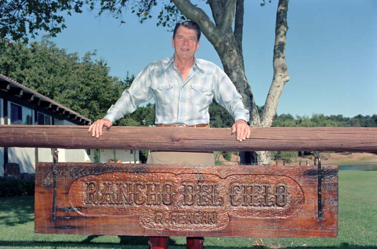 President Reagan standing above a sign, reading "Rancho del Cielo."