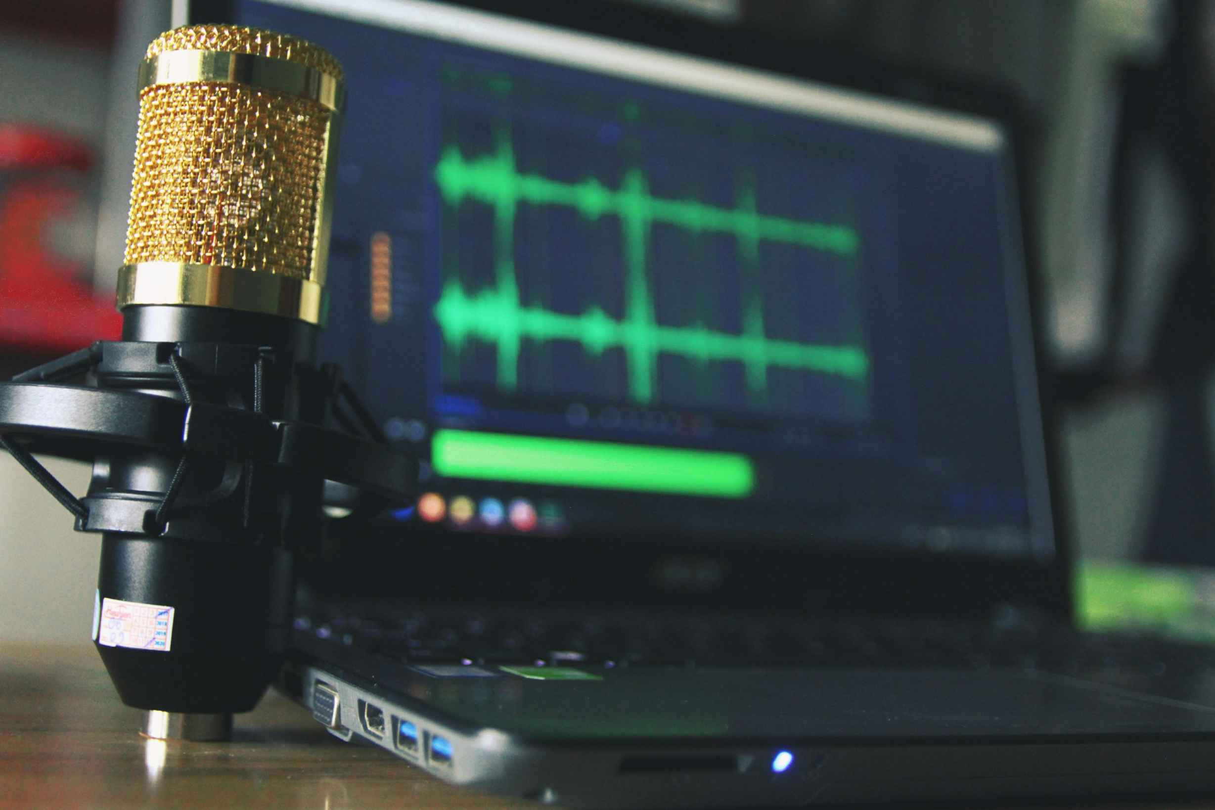 condenser microphone next to a laptop screen showing audio recording for a stream