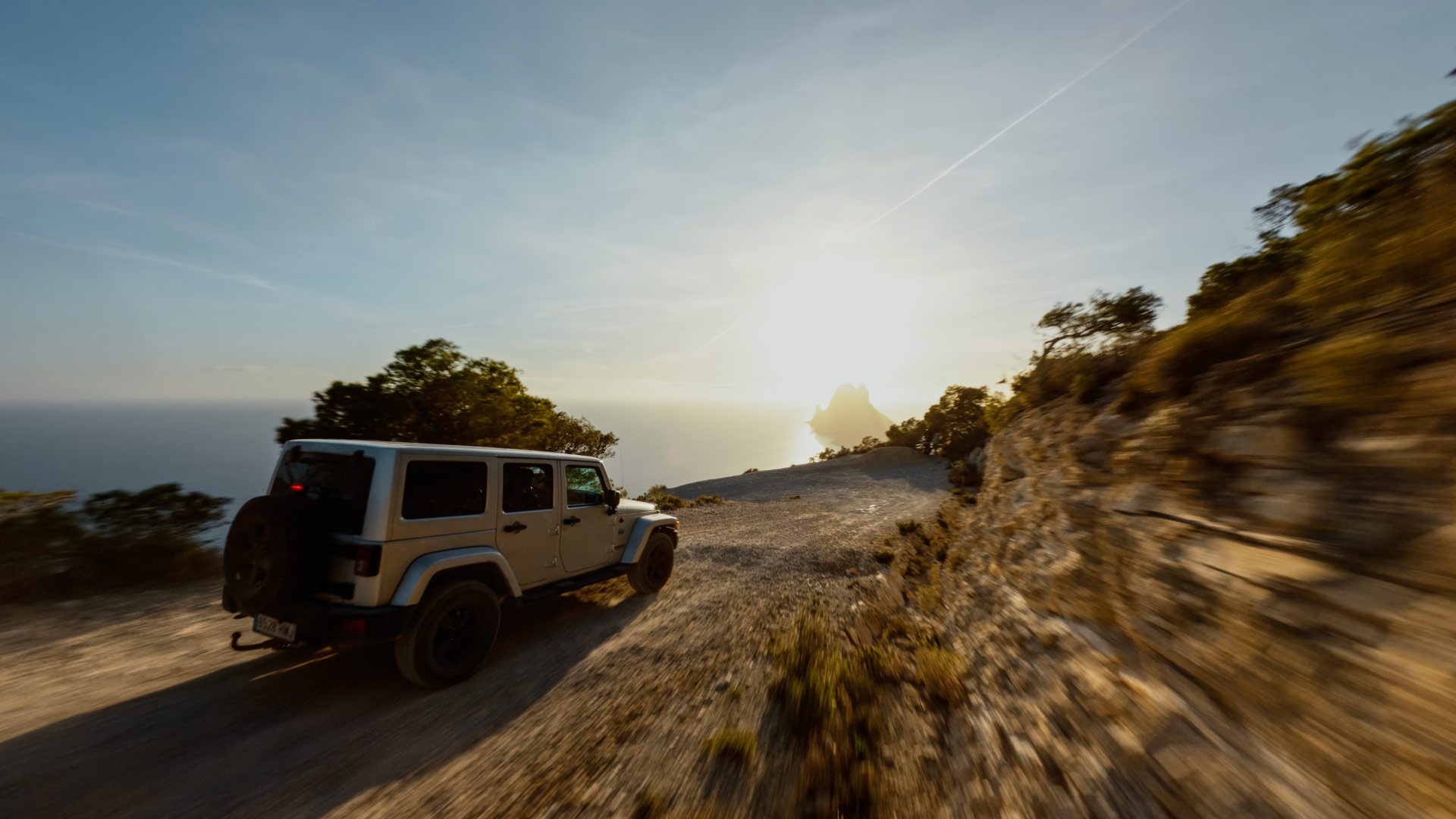 Jeep Wrangler driving coastal Ibiza landscape road representing private guest transport and island mobility.