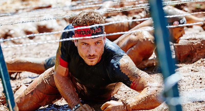 Photo of a man crawling under barbwire in the mud
