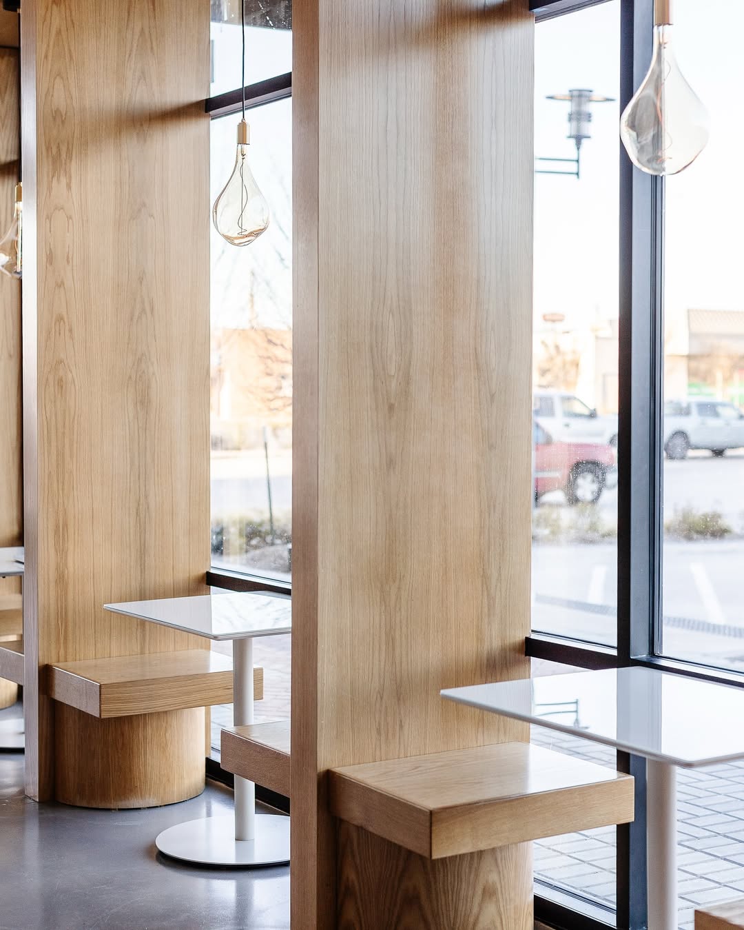 Minimalist seating area inside La Souq café in Dallas featuring warm wood booths, clean-lined tables, pendant lighting, and natural light from large street-facing windows.