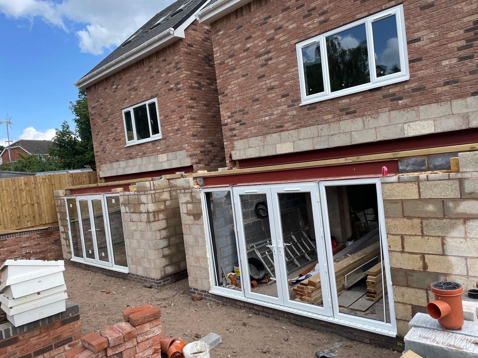A brick building with large glass doors, a window above, and construction materials nearby under a blue sky.