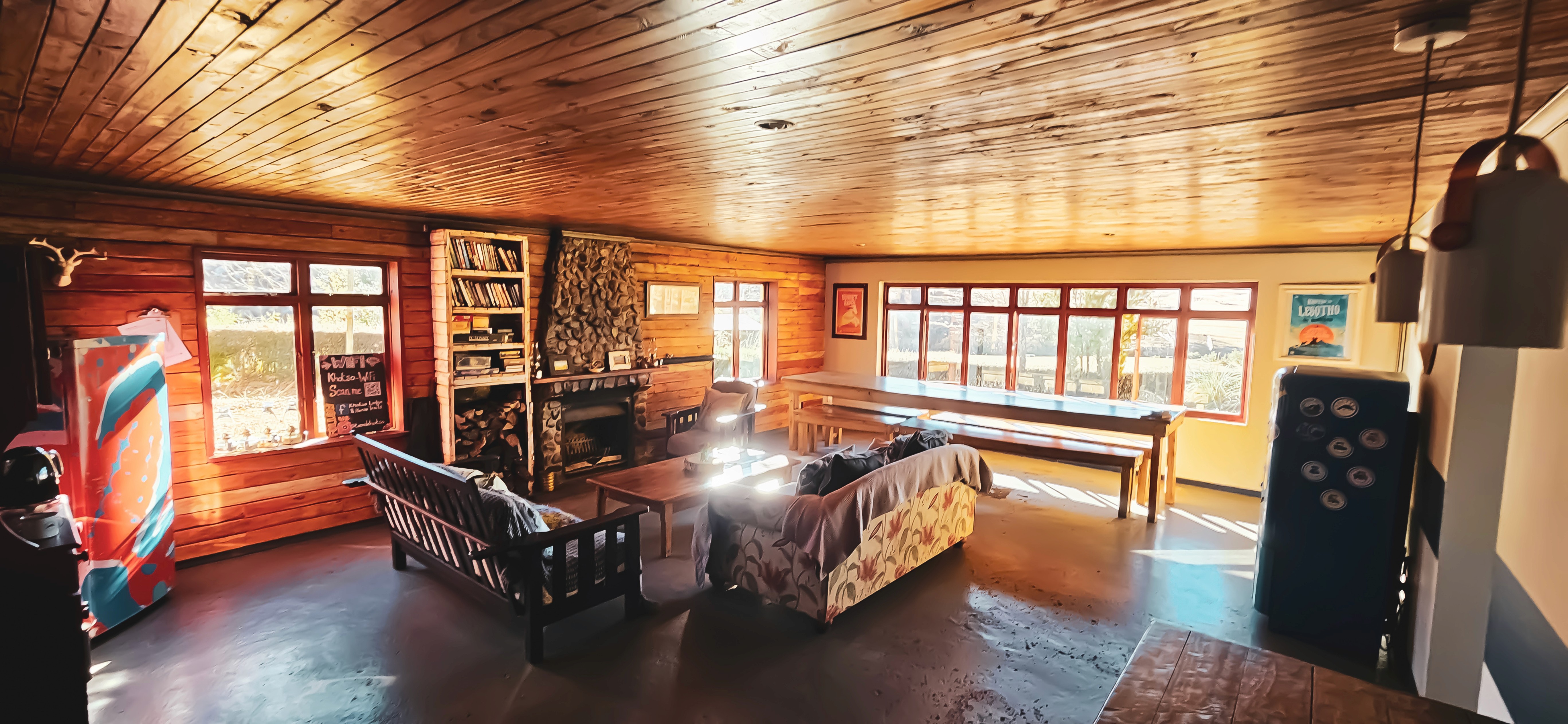 A wood-paneled common area in a hostel with sunlight streaming in through the windows