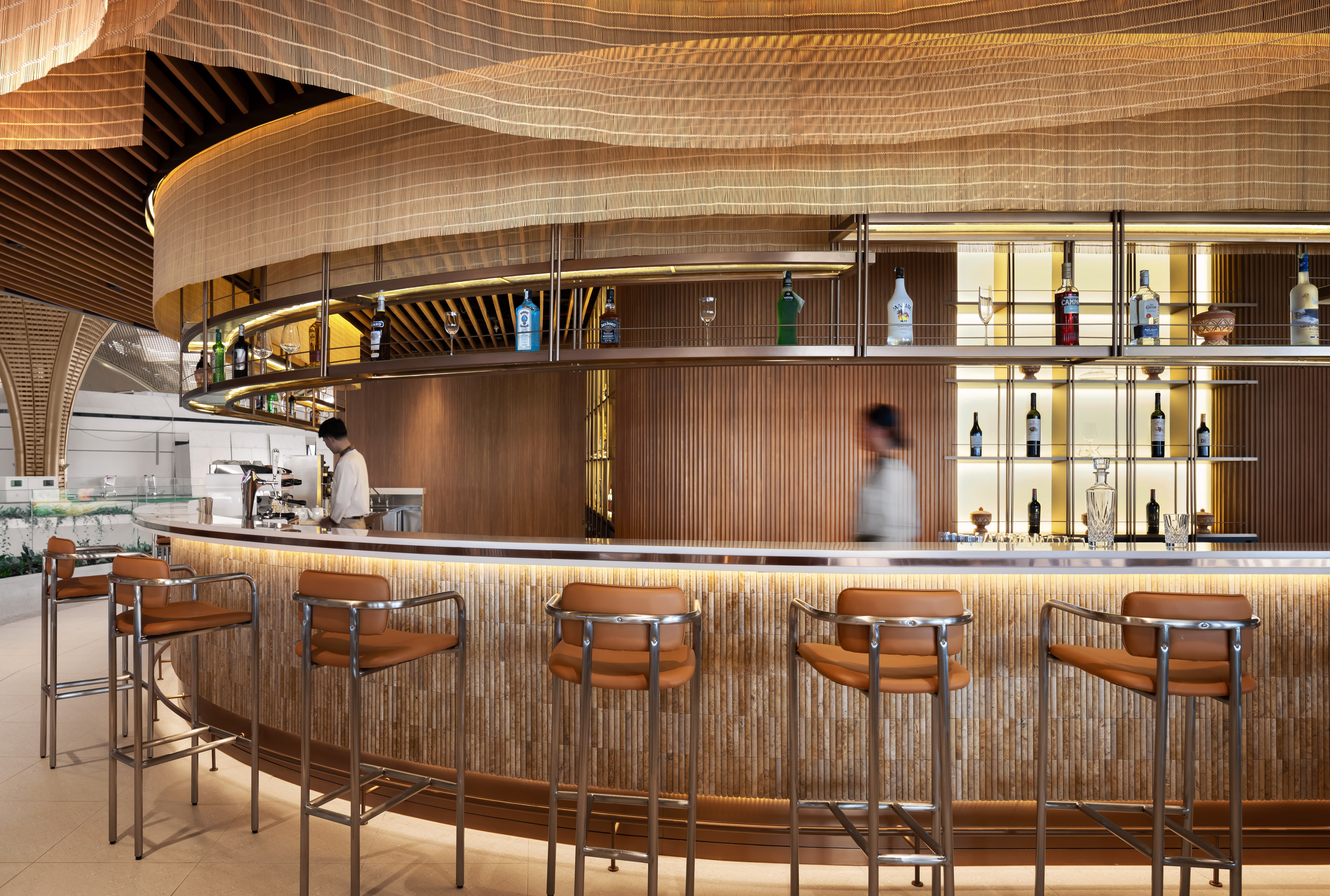 modern-terrazzo-bar-techo-airport Wide view of the elegantly lit circular bar at Malis Restaurant showcasing timber panels and silk installations.
