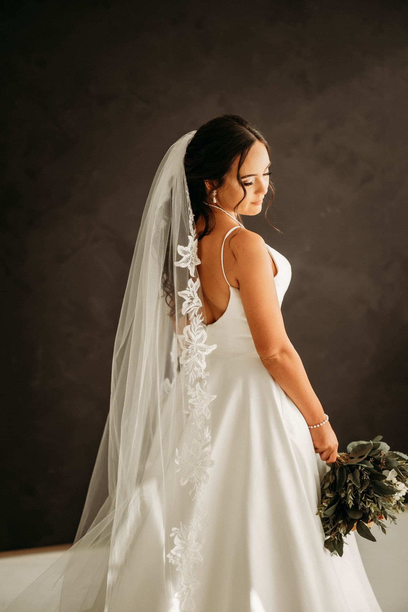 The bride stands in profile, her veil falling elegantly as she holds a bouquet, during a bridal shoot at Revelator Studio, a natural light studio in Shreveport.