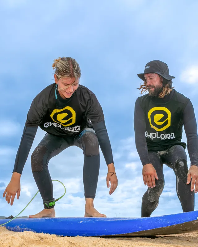 Estudiante de surf practicando la postura en la arena con la guía de un instructor en Explora Watersports Tarifa. Aprende técnicas básicas para mejorar tu surf en un ambiente profesional y seguro.