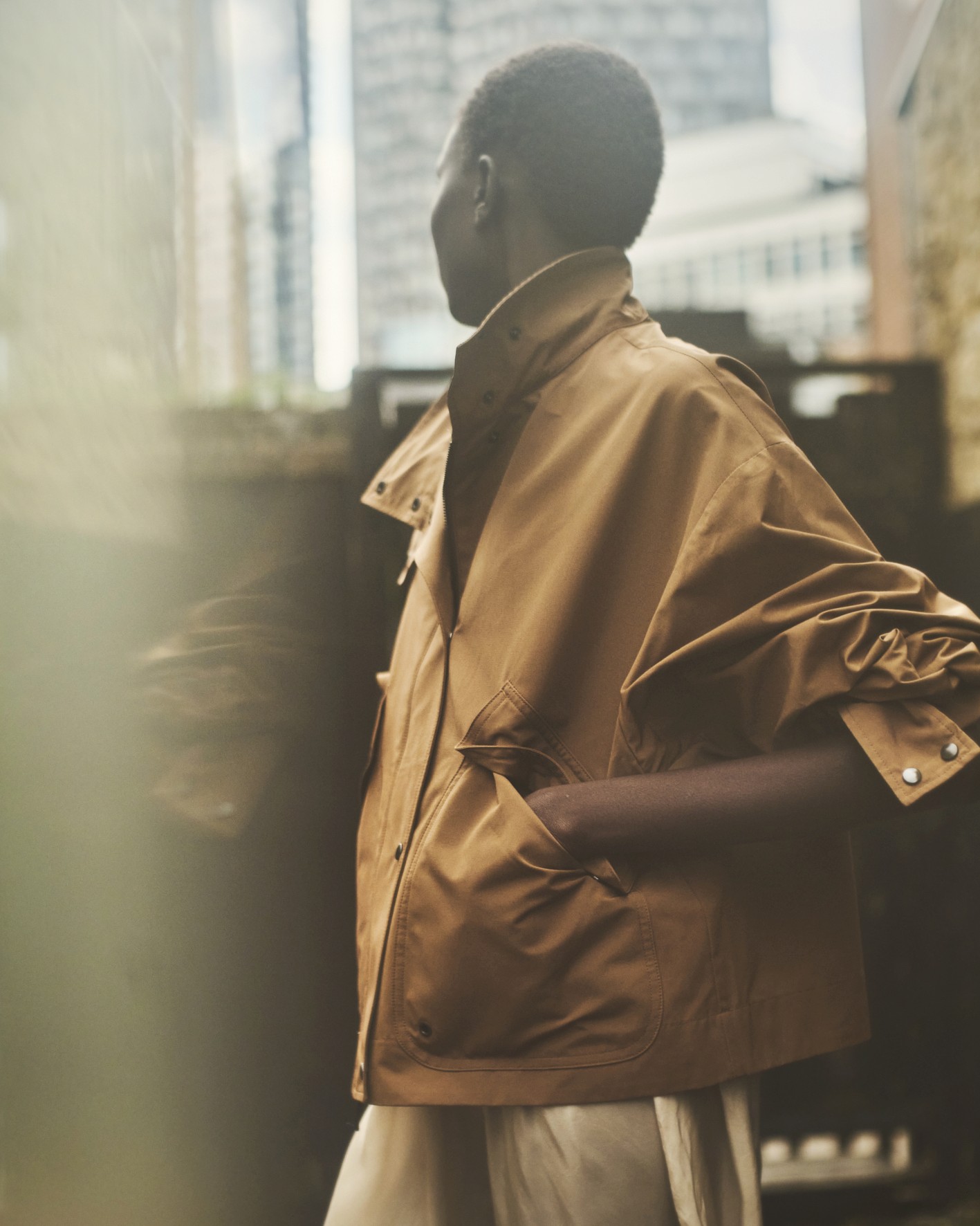 Avec des grattes ciel en fond flou,une mannequin porte un blouson oversize beige orangé