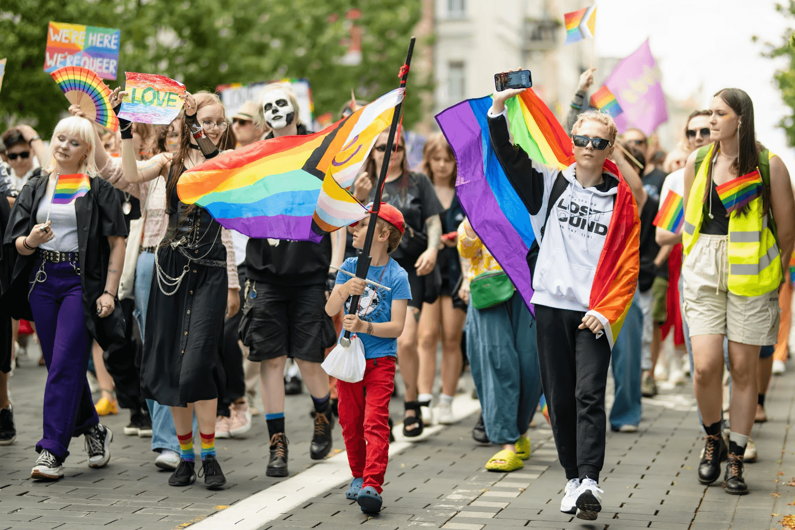 A vibrant crowd marches in a parade, holding rainbow flags and celebrating diversity and inclusion.
