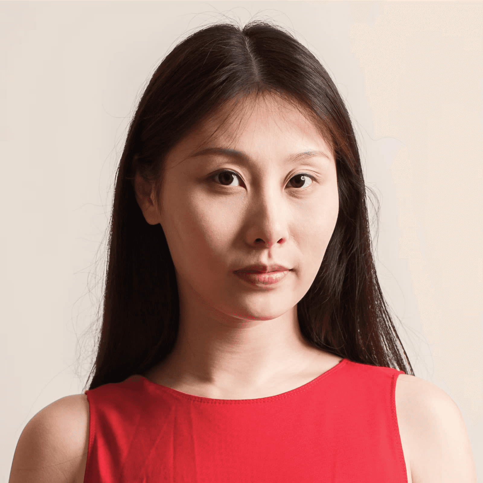 A head-and-shoulders portrait of a woman with long, straight dark hair and a neutral expression, looking directly at the camera. She is wearing a bright red sleeveless top against a simple, light cream-colored background.