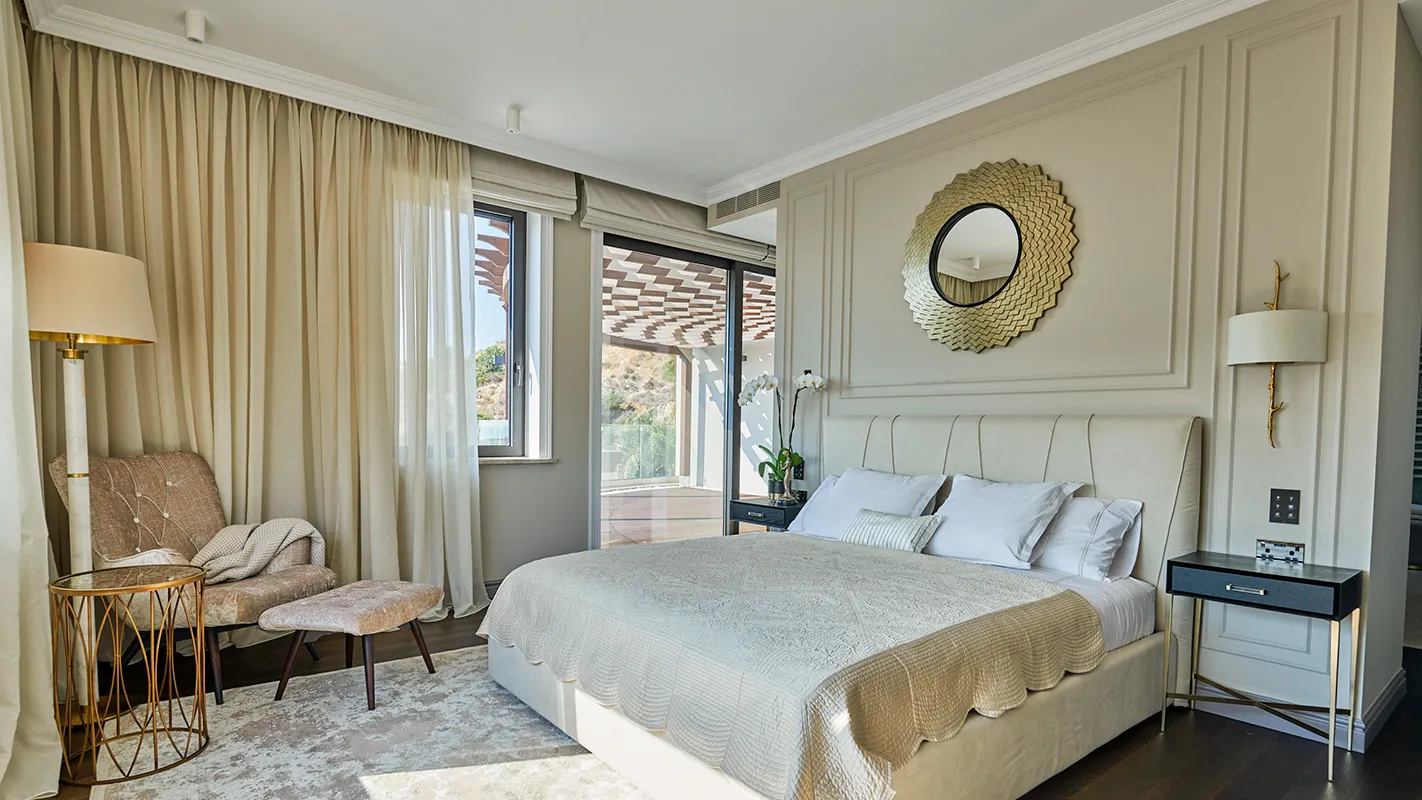 Villa Belmare bedroom with neutral tones, upholstered headboard, and statement round mirror above the bed