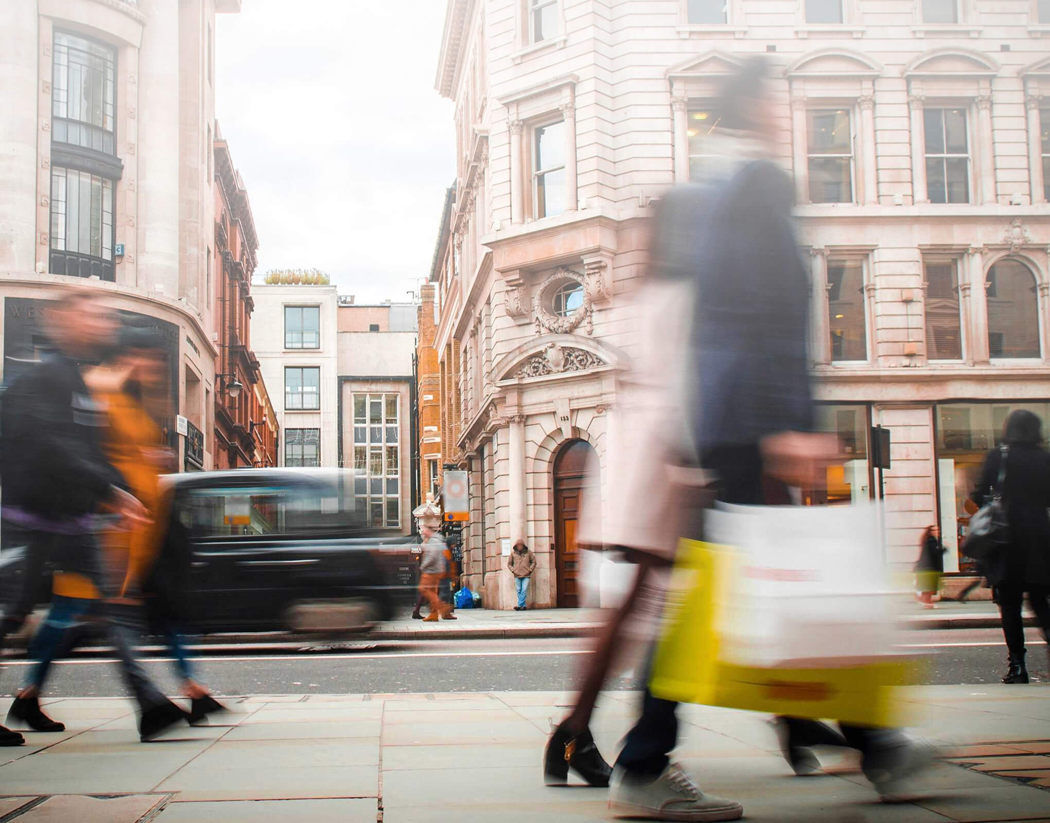 Blurred shoppers walking past city buildings with shopping bags