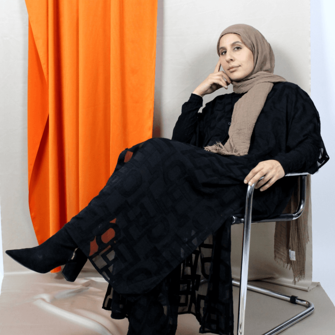 Three people in conversation with warm lighting, including a person wearing a hat and another person wrapped in what appears to be a textured shawl or sweater.