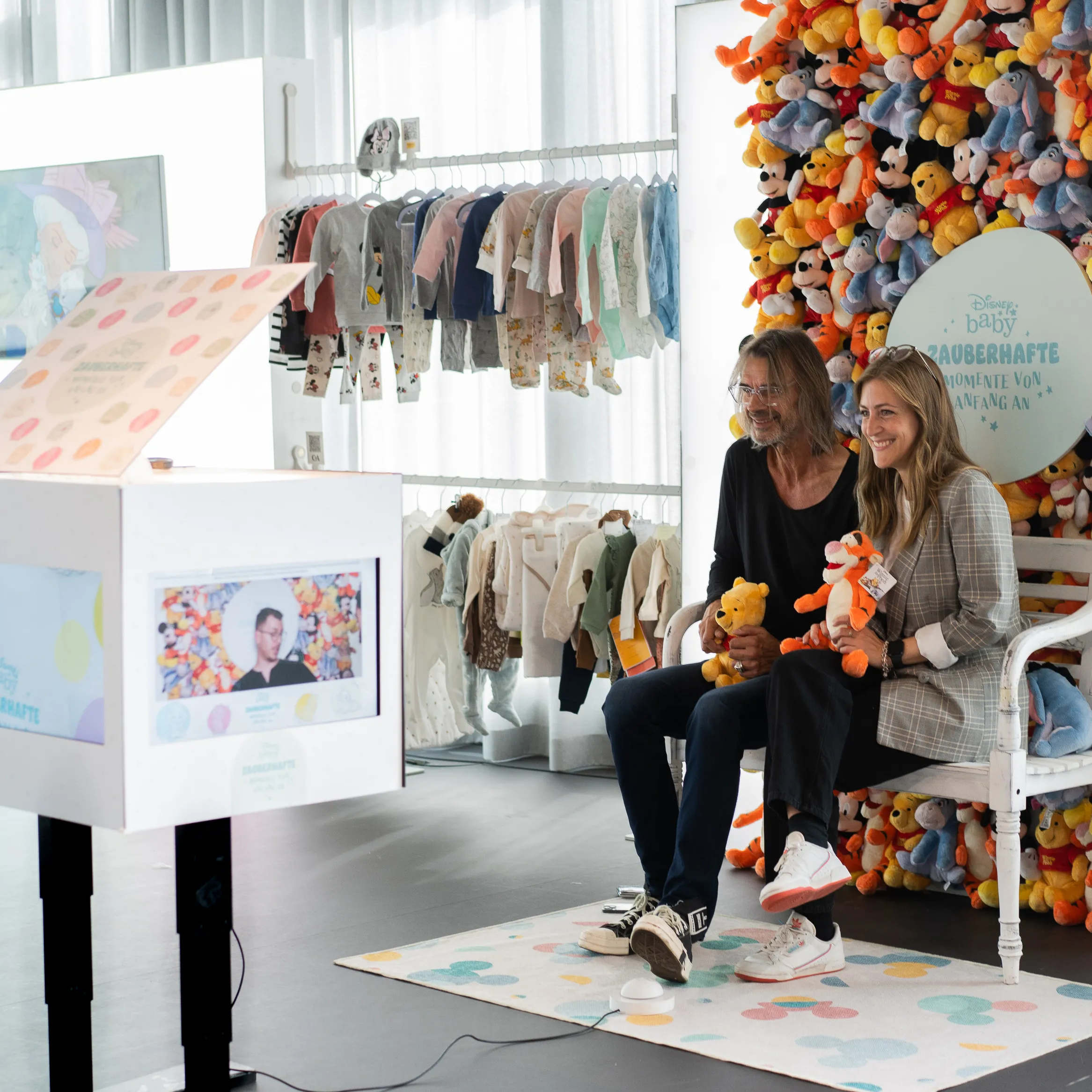 Paar sitzt vor einer gebrandeten SnapCube Fotobox in einer Disney Baby Erlebniswelt