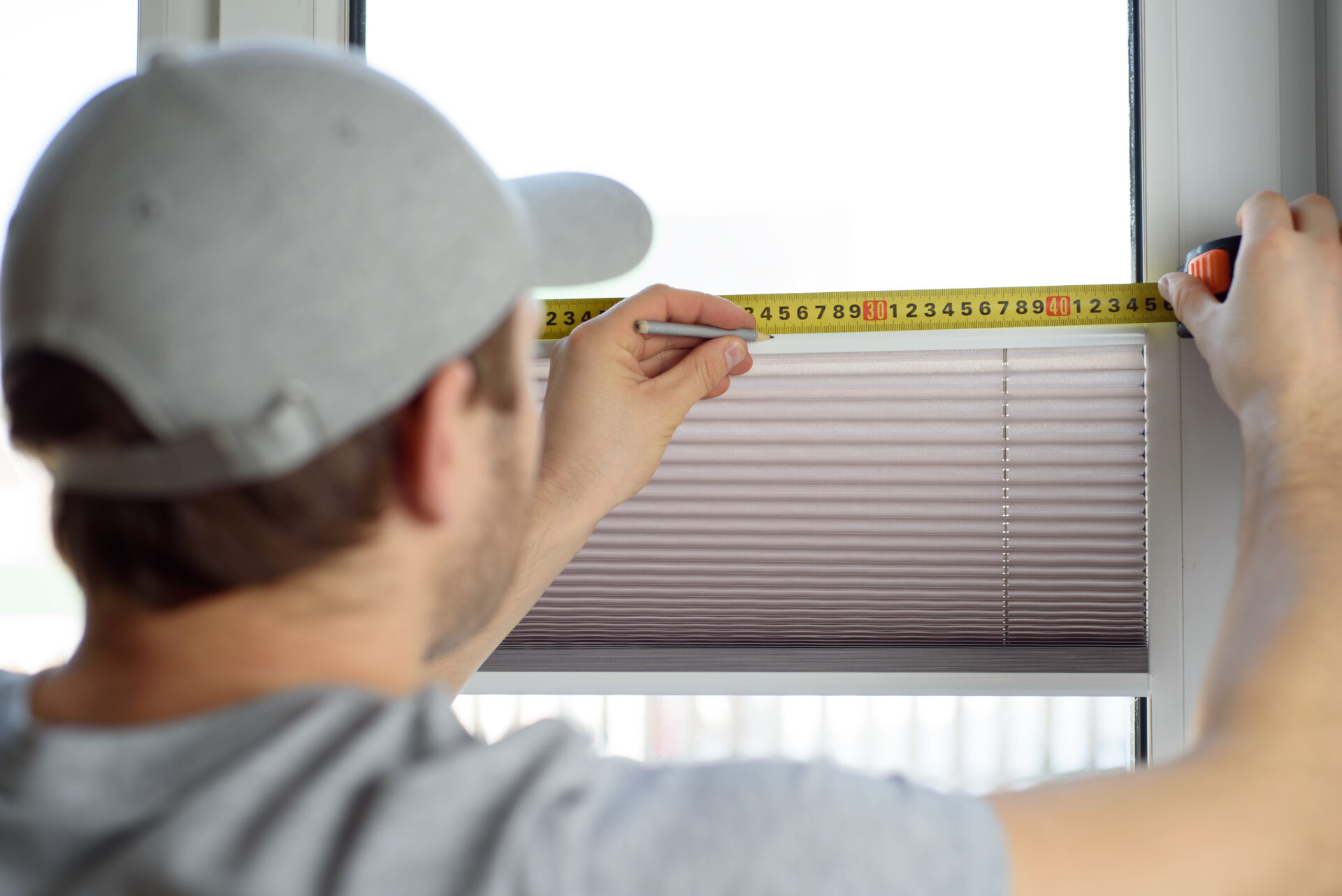 Man installing gray Somfy blinds on the window. Wholesale Blind Factory