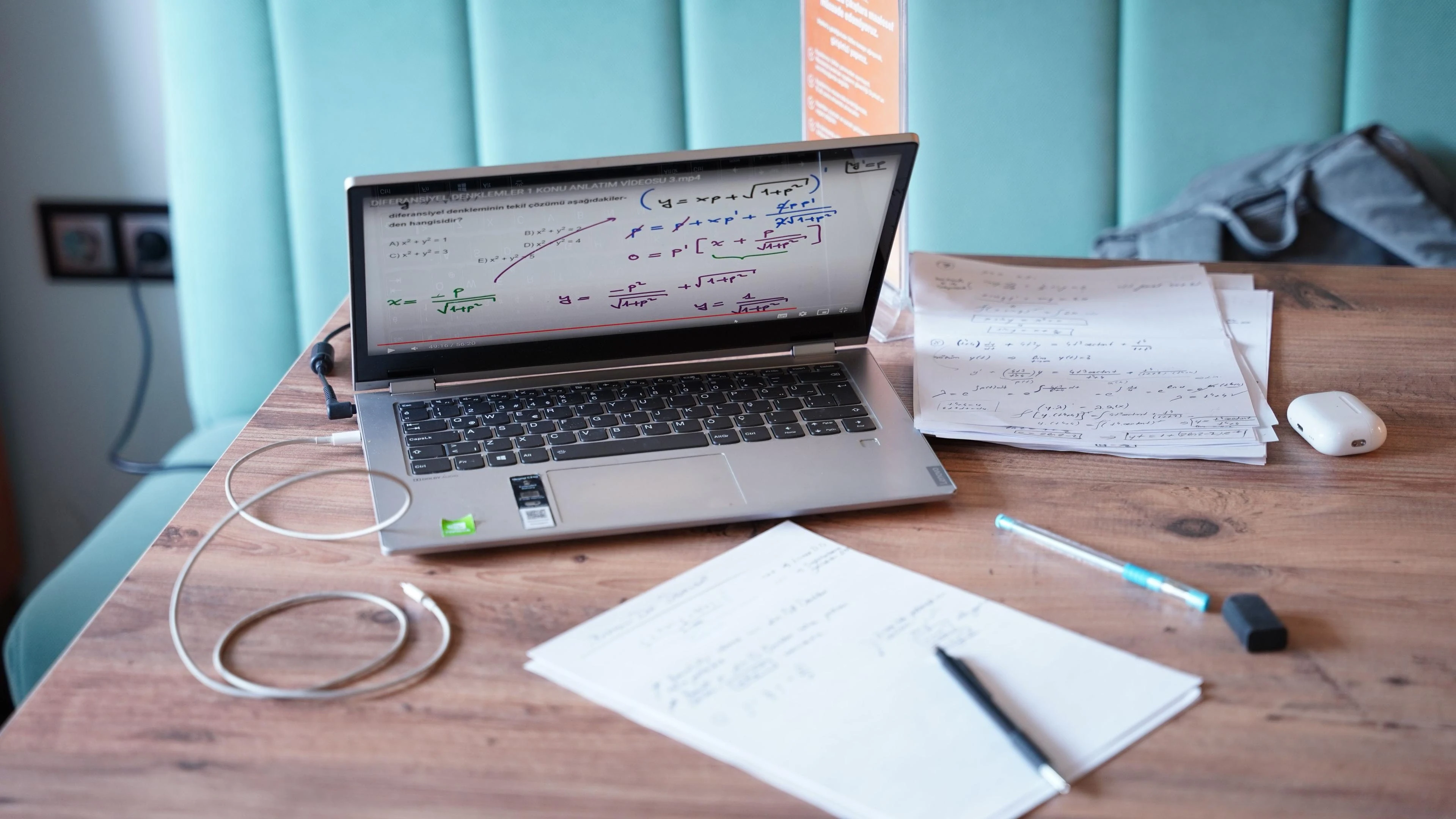 Laptop displaying a differential equations lesson beside handwritten math notes, representing the mathematical foundations behind optimization modeling