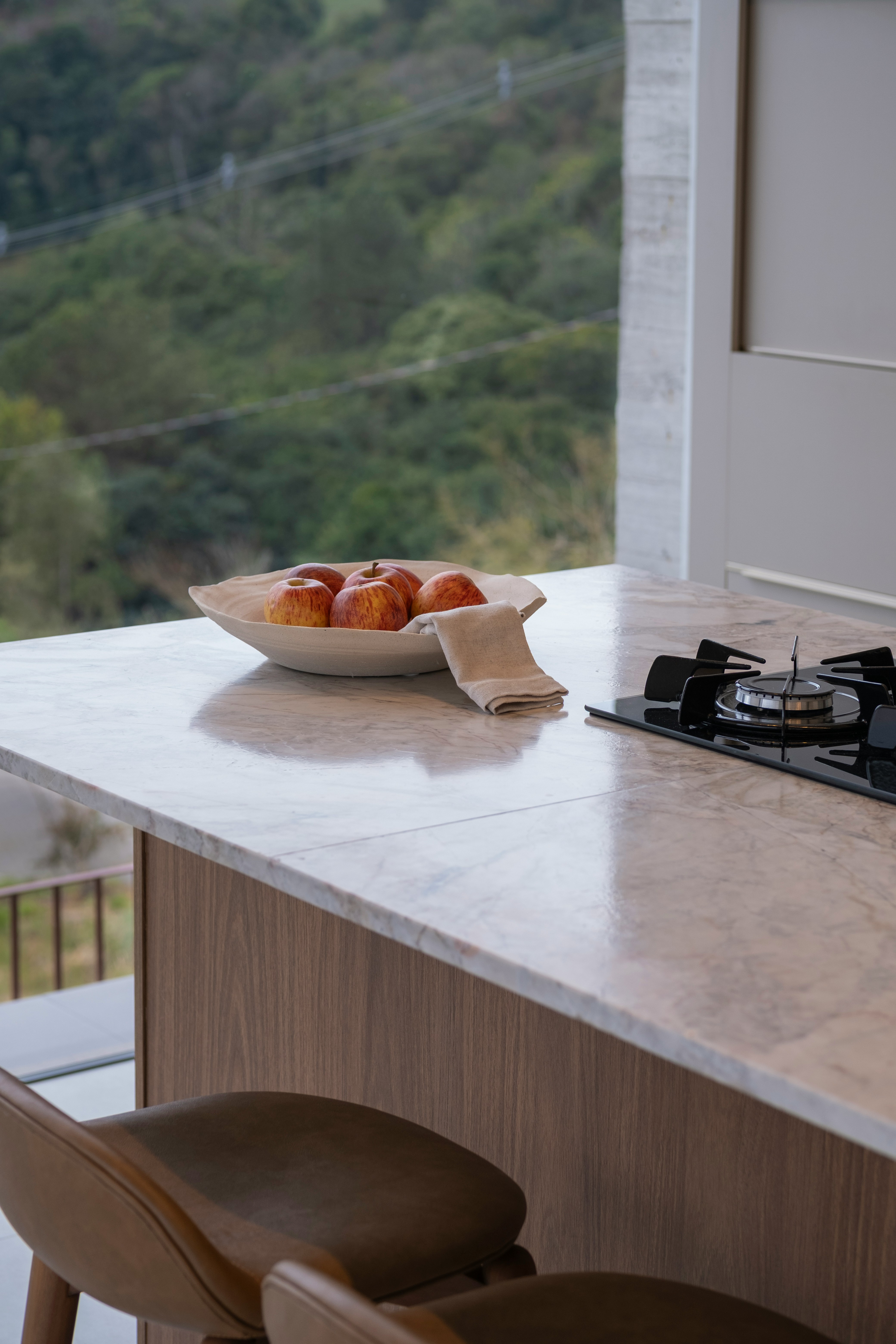 Bowl of apples on marble countertop with stove.