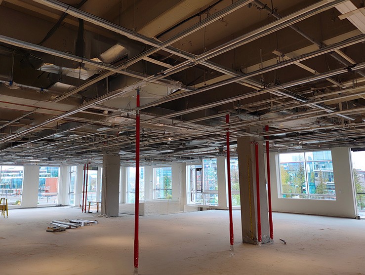  a spacious, industrial-style interior under renovation, featuring exposed ceiling beams, red support poles, and large windows allowing natural light to illuminate the construction area.