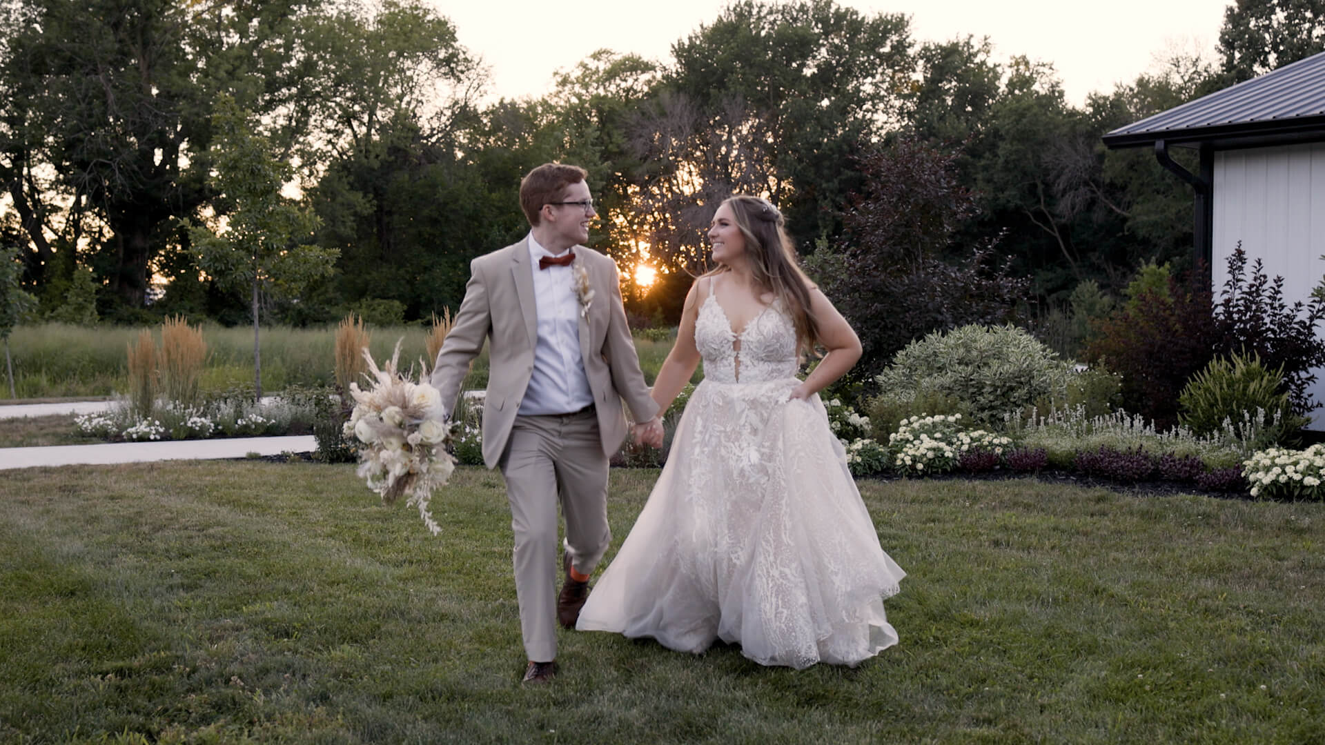 A bride and groom look at each other lovingly while walking in front of a sunset