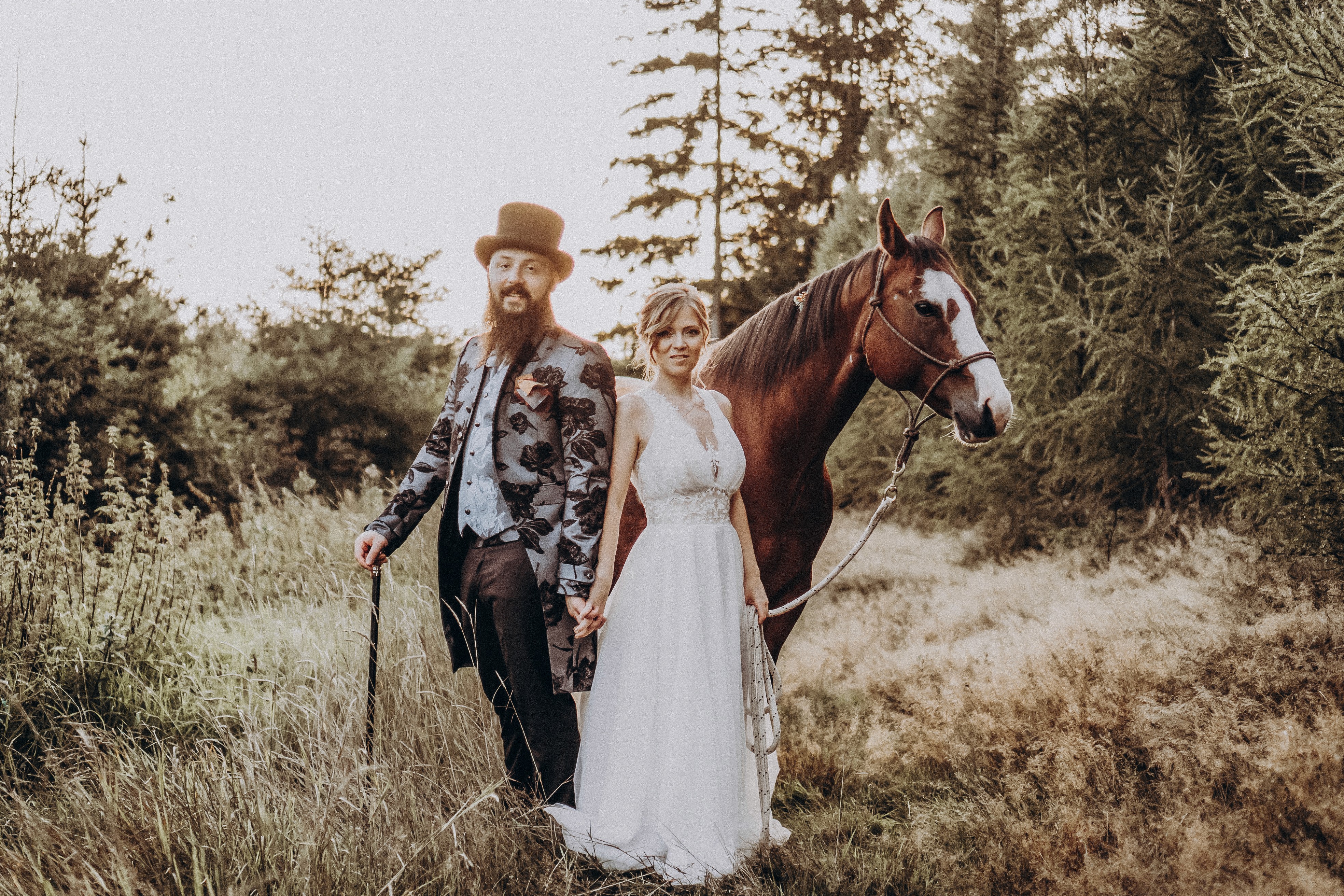 Bräutigam mit Zylinder hält ein Pferd auf einem Feld in Niederbayern – Hochzeitsfotograf Anastasiia Teske