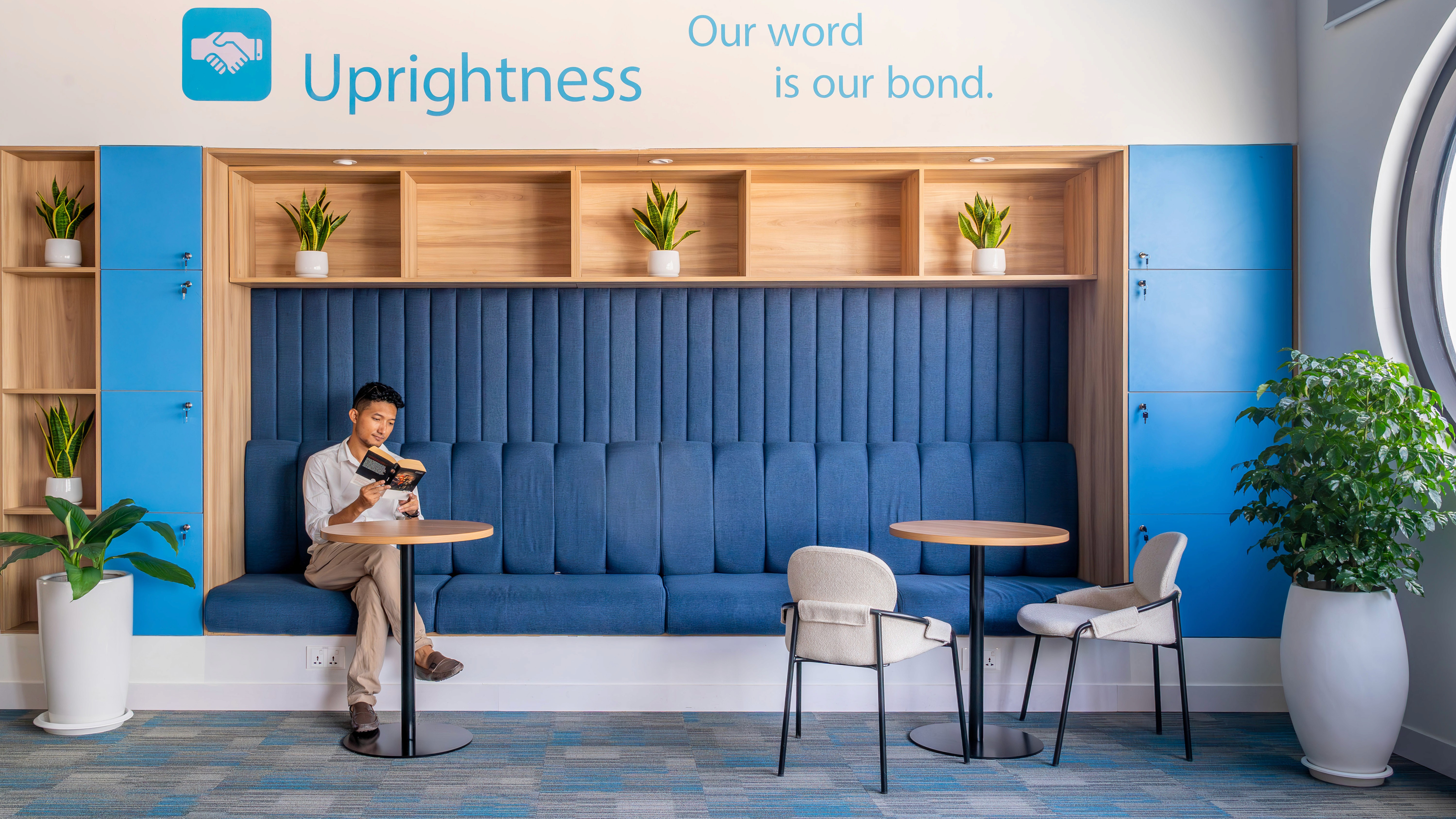 Acoustic focus booth with upholstered backrest, integrated shelving, and small tables providing semi-private work settings