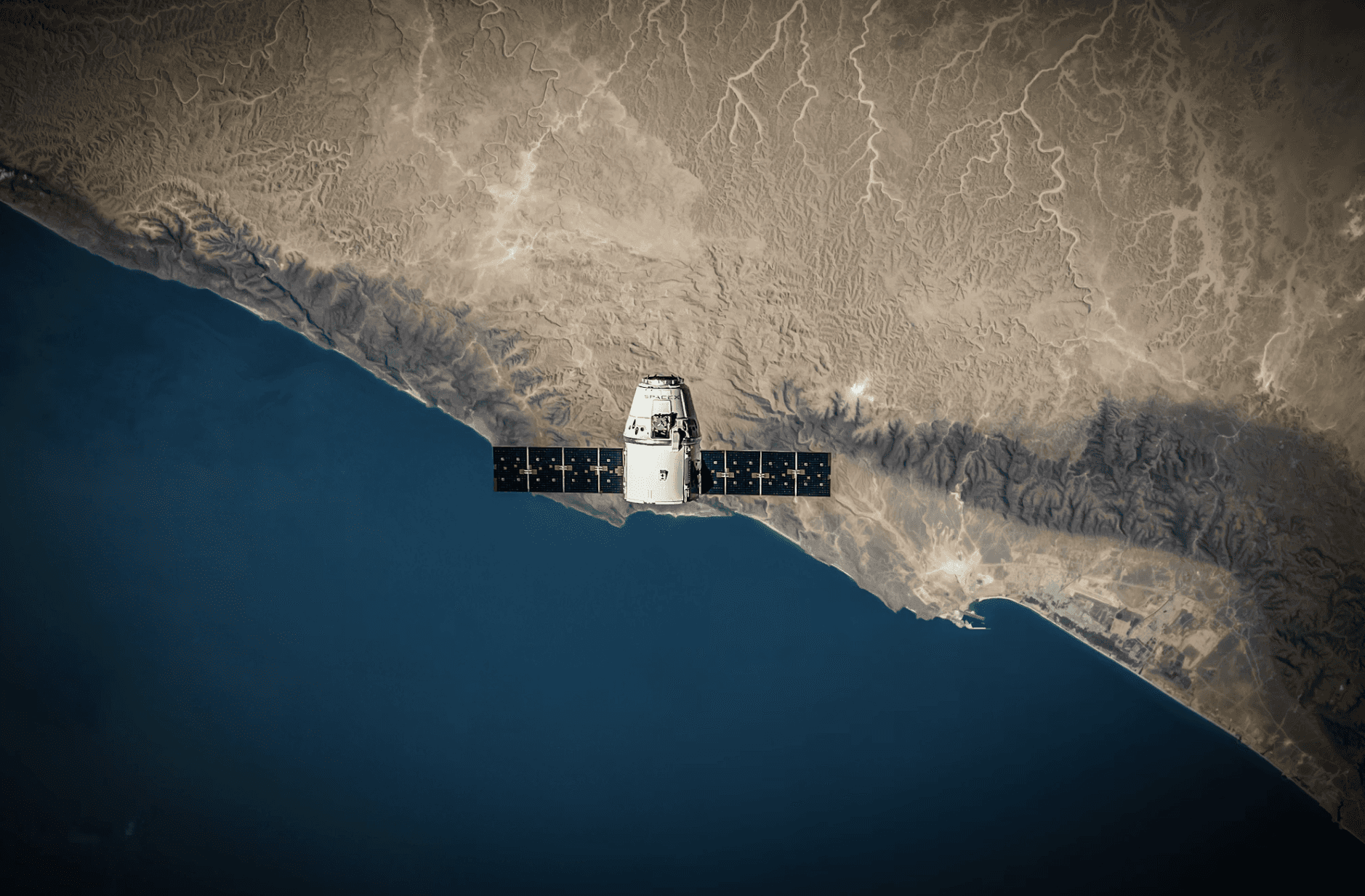 Aerial view of a winding road cutting through rocky terrain and sandy landscape.