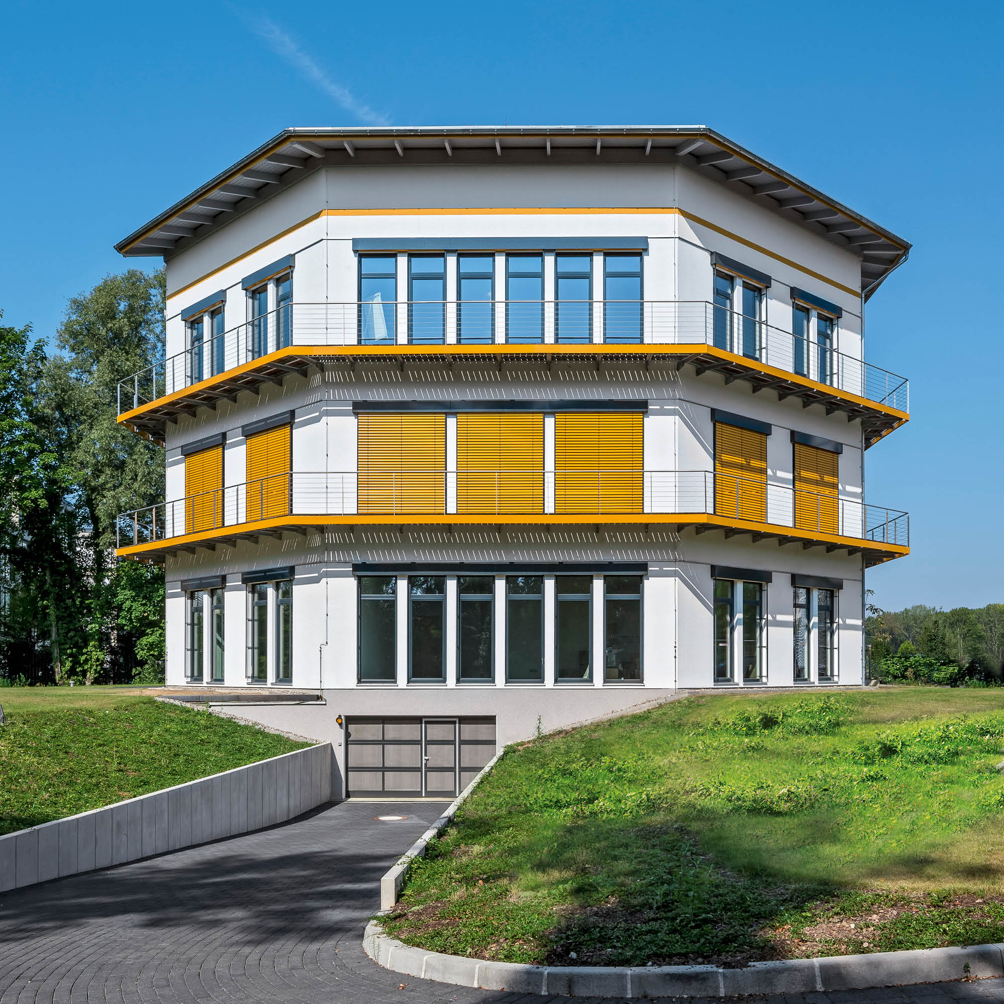 Modernes Gebäude mit mehreren Stockwerken, umlaufenden orangefarbenen Balkonen, weißen Fassaden und gelben Lamellenfenstern.