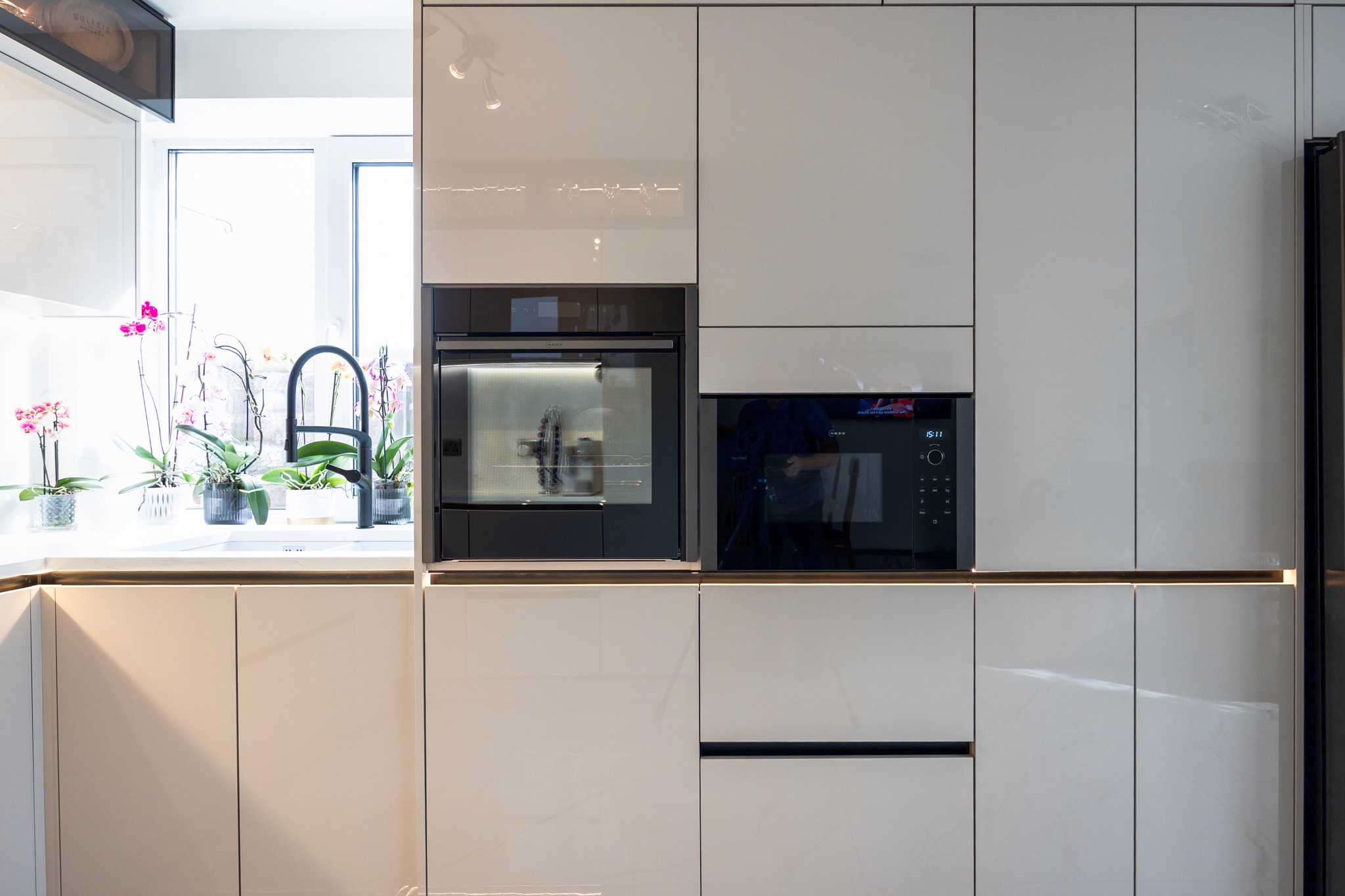 Modern two-story home with large glass windows, warmly lit interiors, and a balcony. Surrounded by trees and a manicured lawn at dusk. Cozy ambiance.