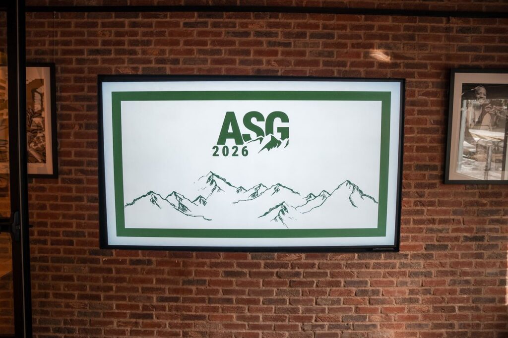 Screen displaying ASG 2026 branding and a mountain illustration on an exposed brick wall
