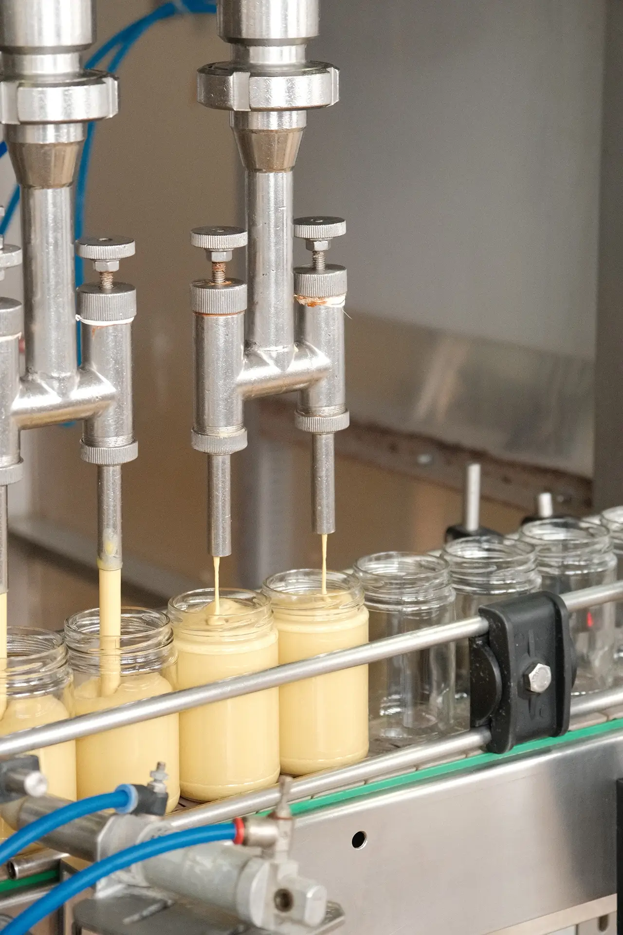 Zautomatyzowany proces napełniania szklanych słoików gęstą musztardą za pomocą precyzyjnych, metalowych dozowników na linii produkcyjnej.