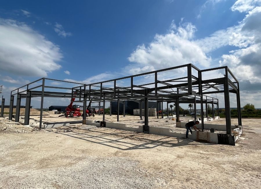 Charpente en acier en cours de montage sur chantier ouvert, ciel partiellement nuageux.