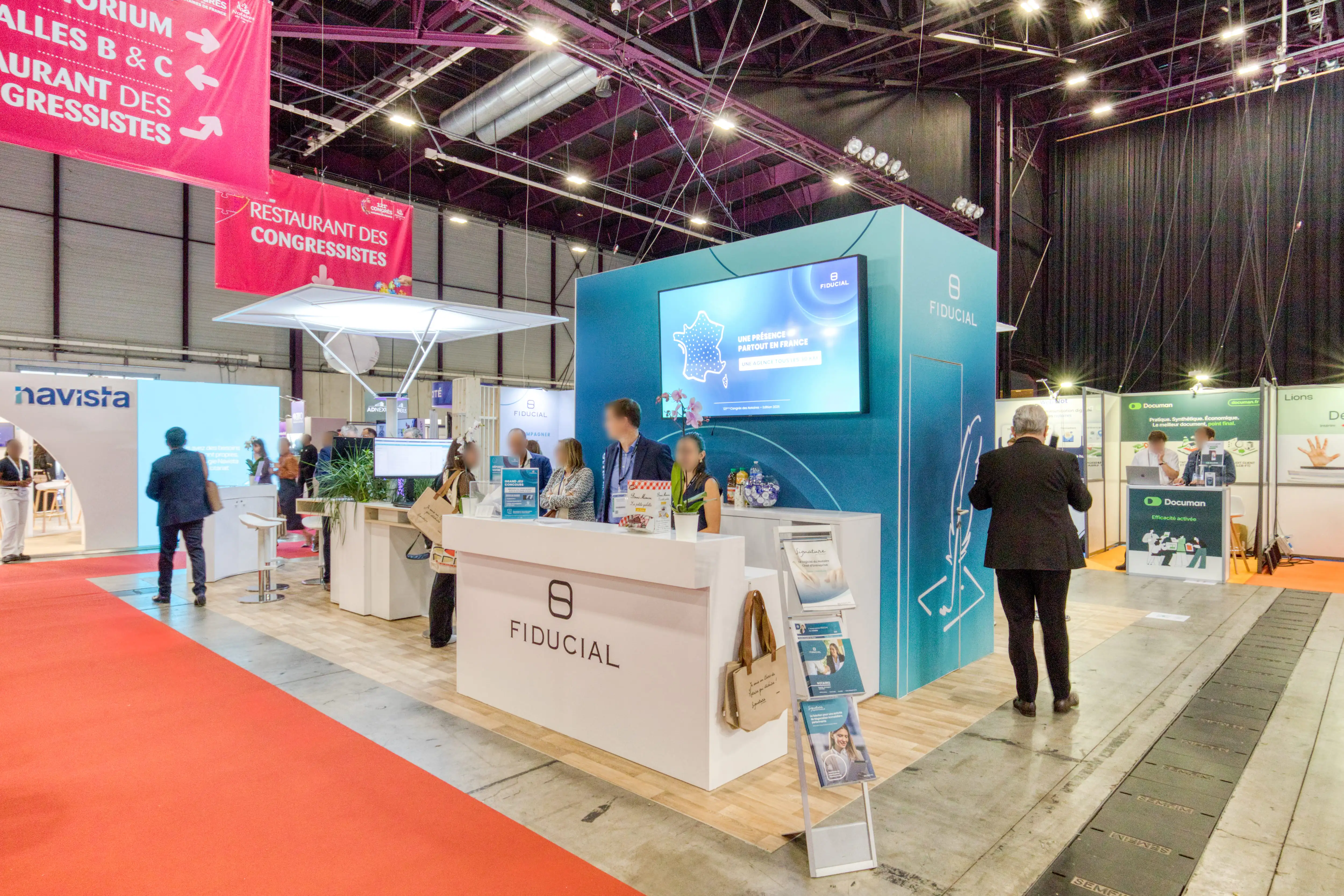 Stand Fiducial conçu par Expace au Congrès des Notaires 2025, avec comptoir blanc et grand mur bleu